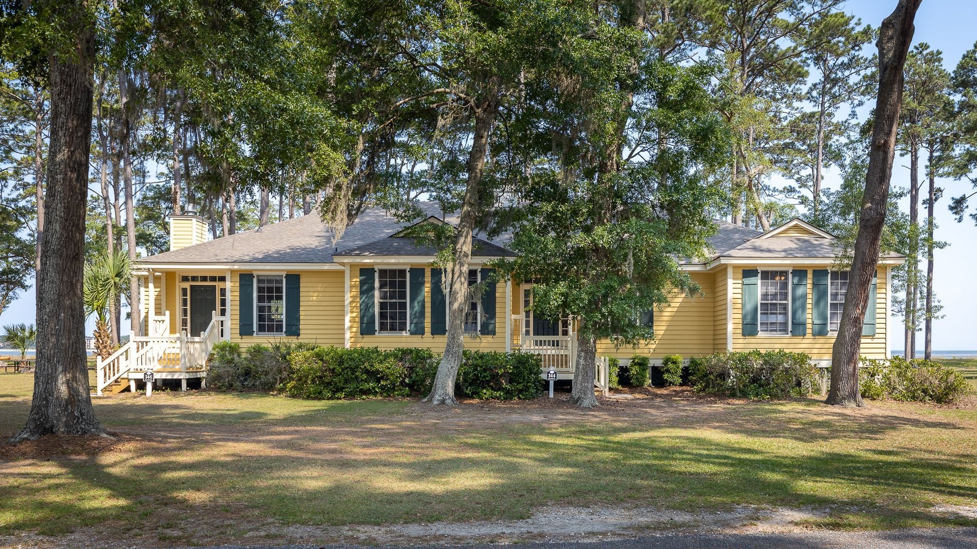 A large yellow house with blue shutters is surrounded by trees.