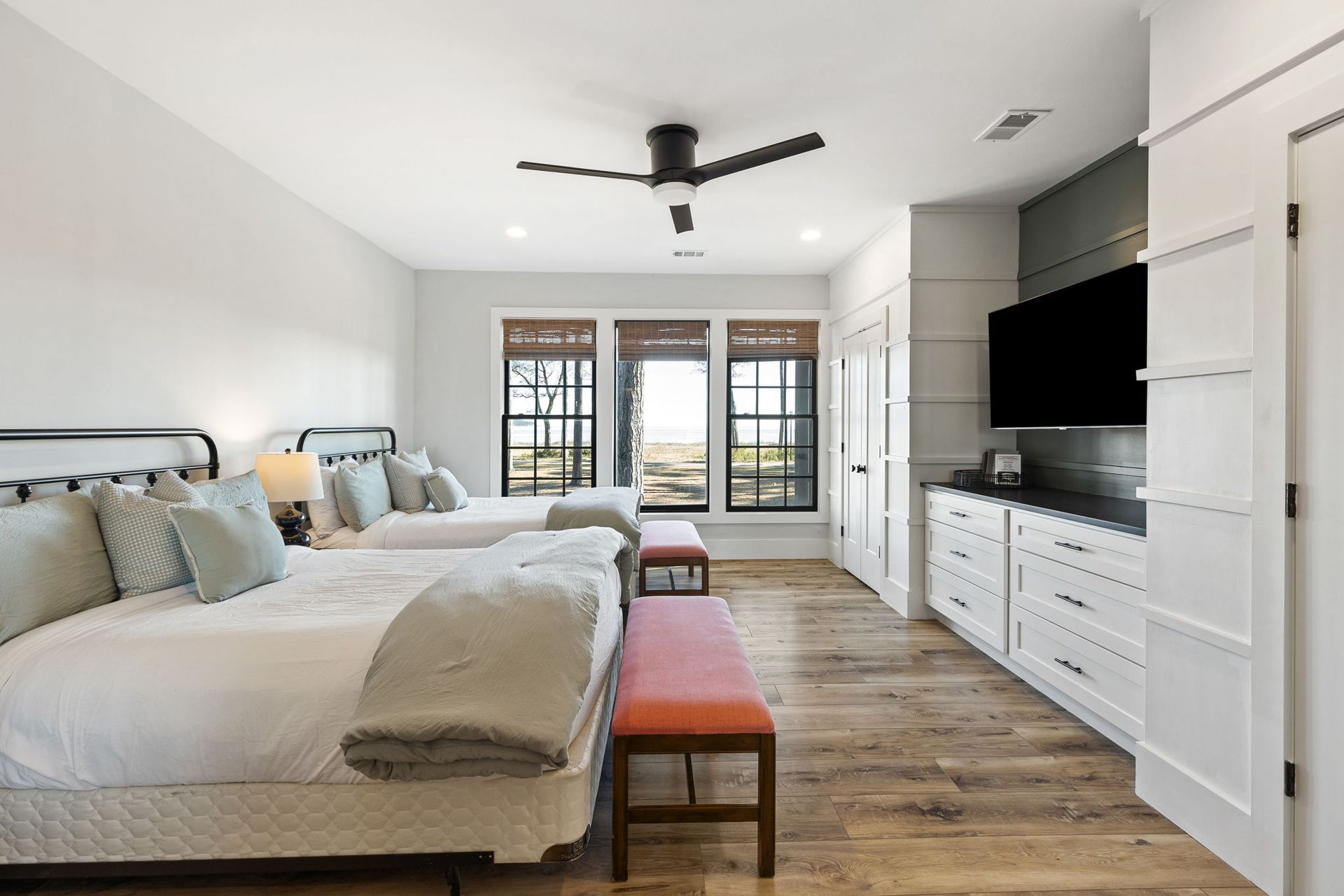A bedroom with two beds , a bench , a television and a ceiling fan.