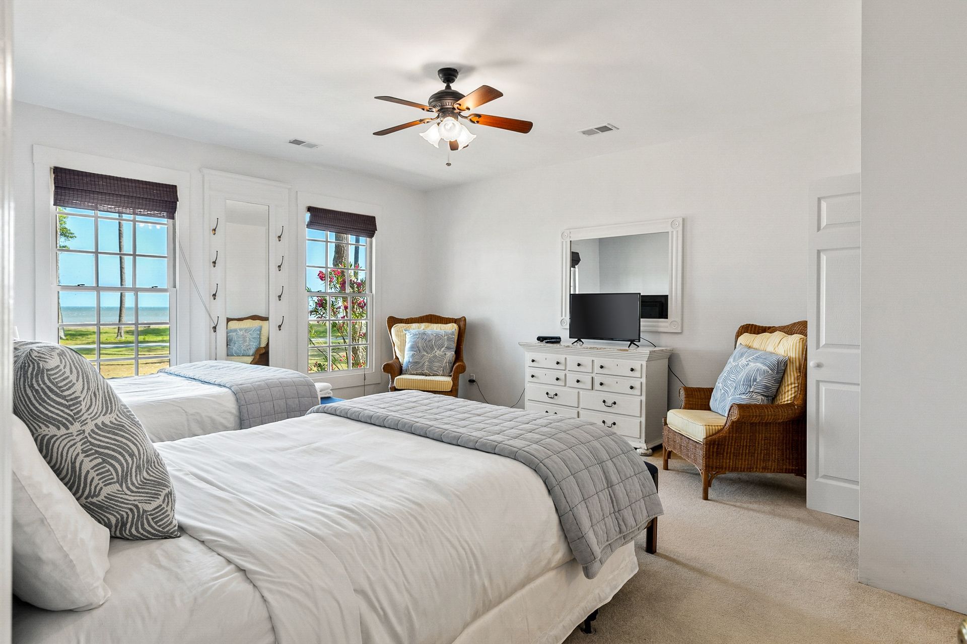A bedroom with two beds , a dresser , a chair , a television and a ceiling fan.