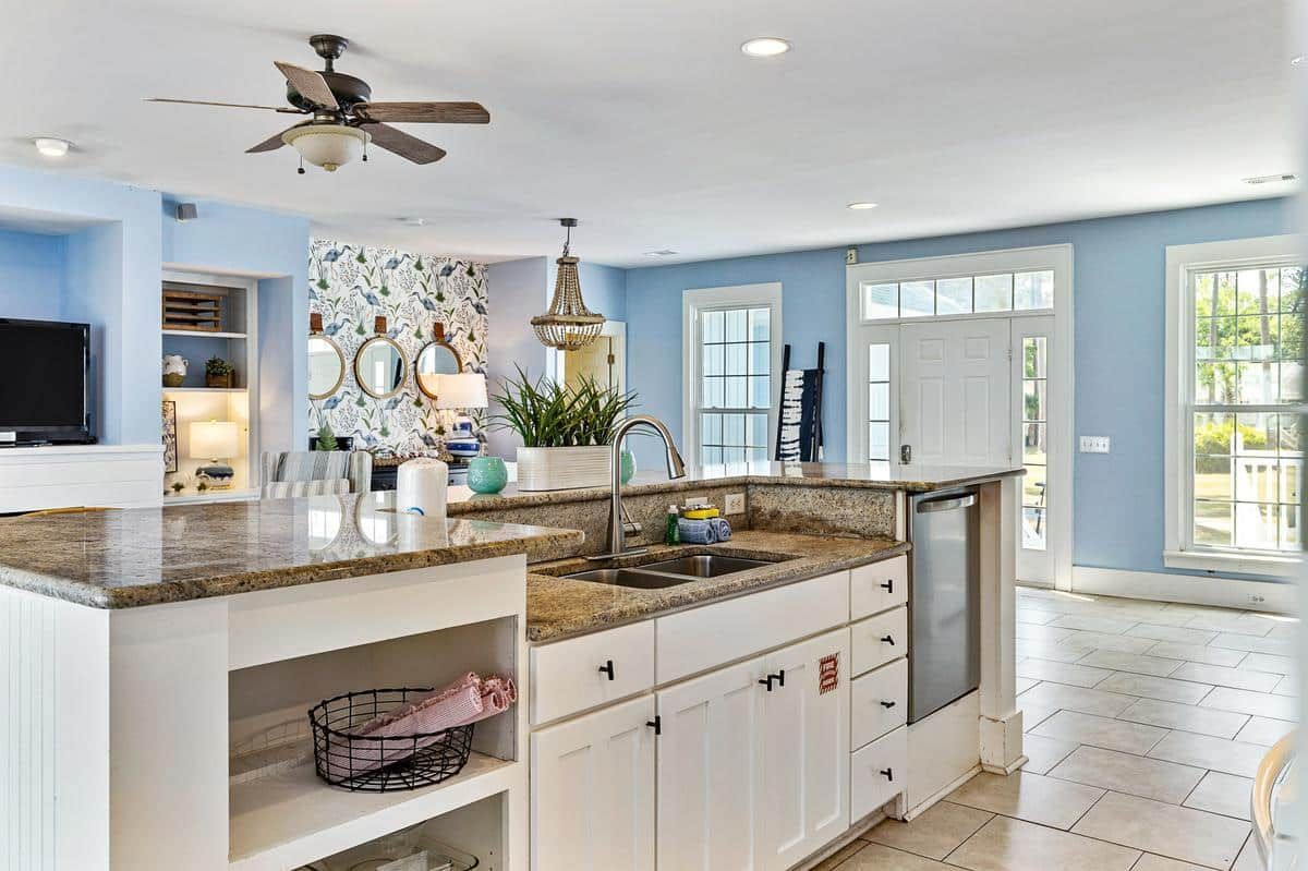 A kitchen with white cabinets , granite counter tops , a sink and a ceiling fan.
