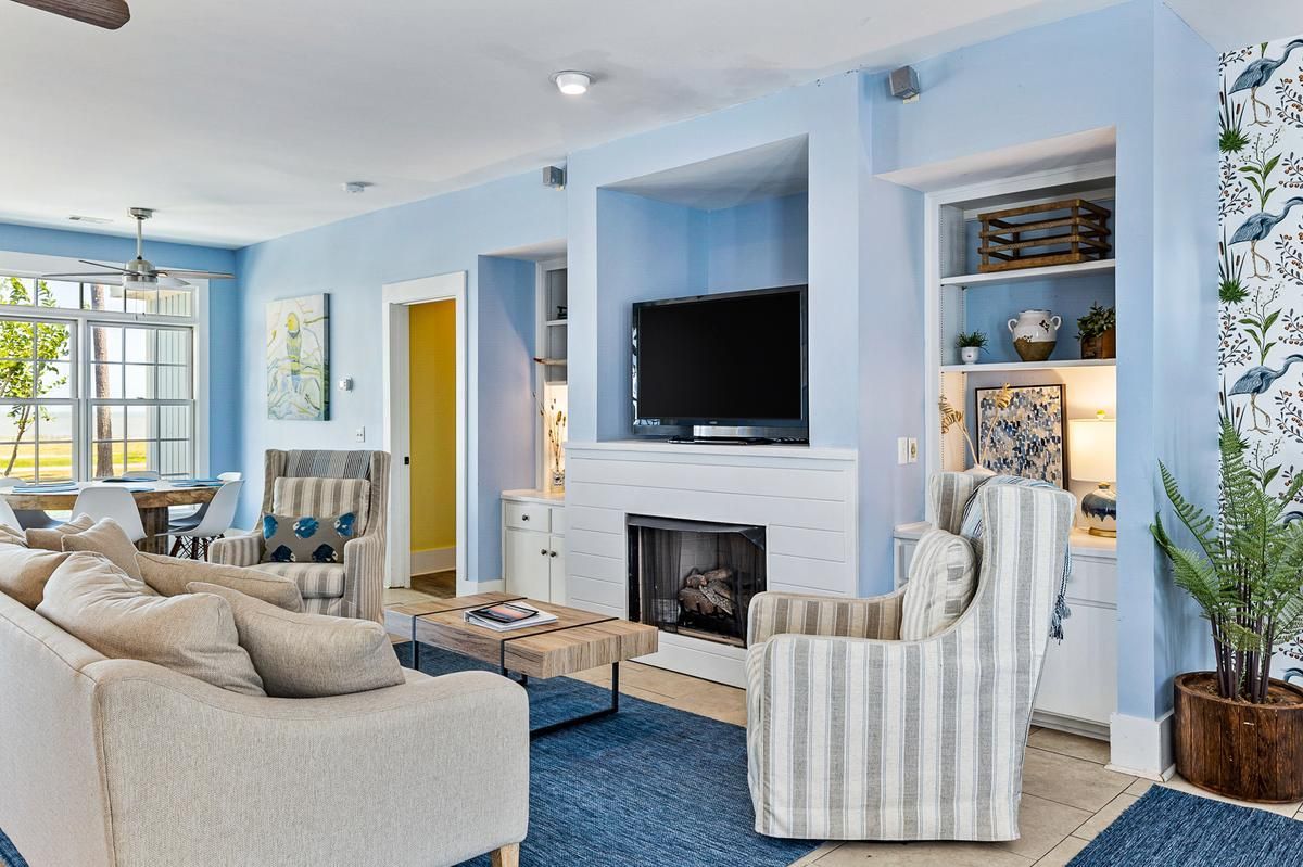 A living room with blue walls , white furniture , a fireplace and a flat screen tv.