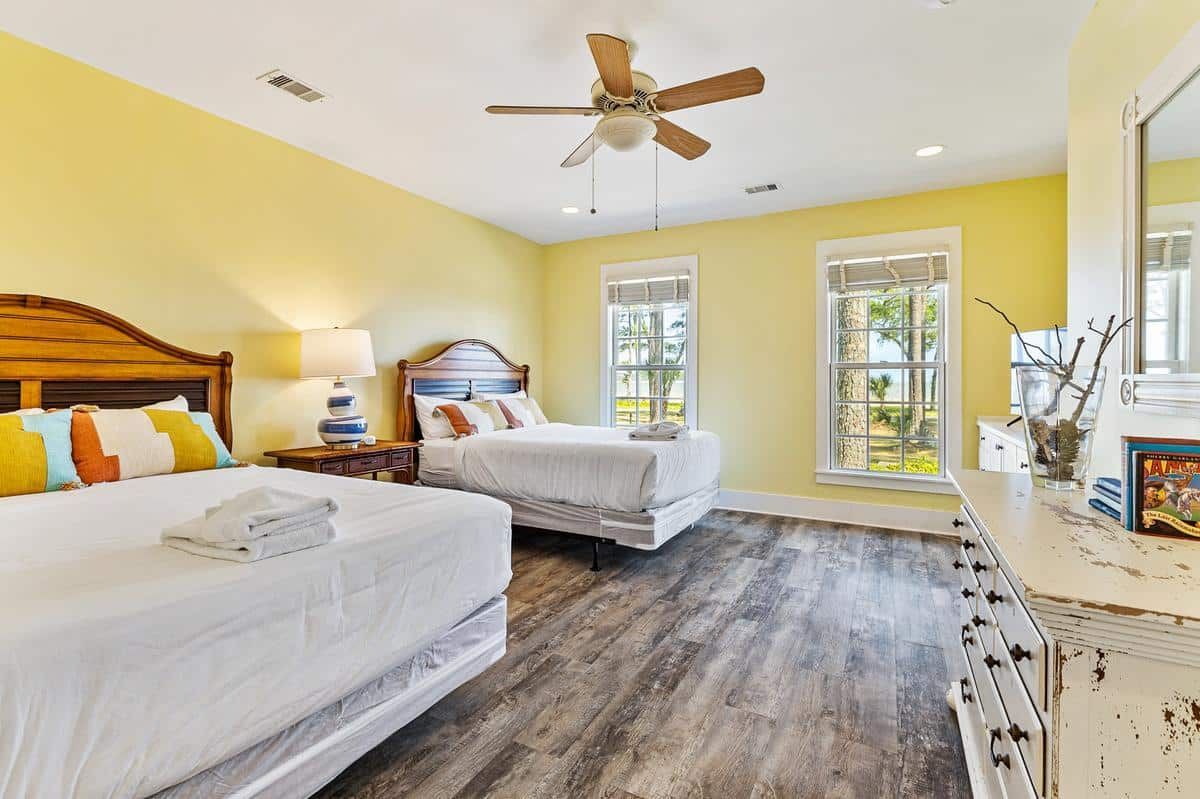 A bedroom with two beds , a dresser , a mirror and a ceiling fan.