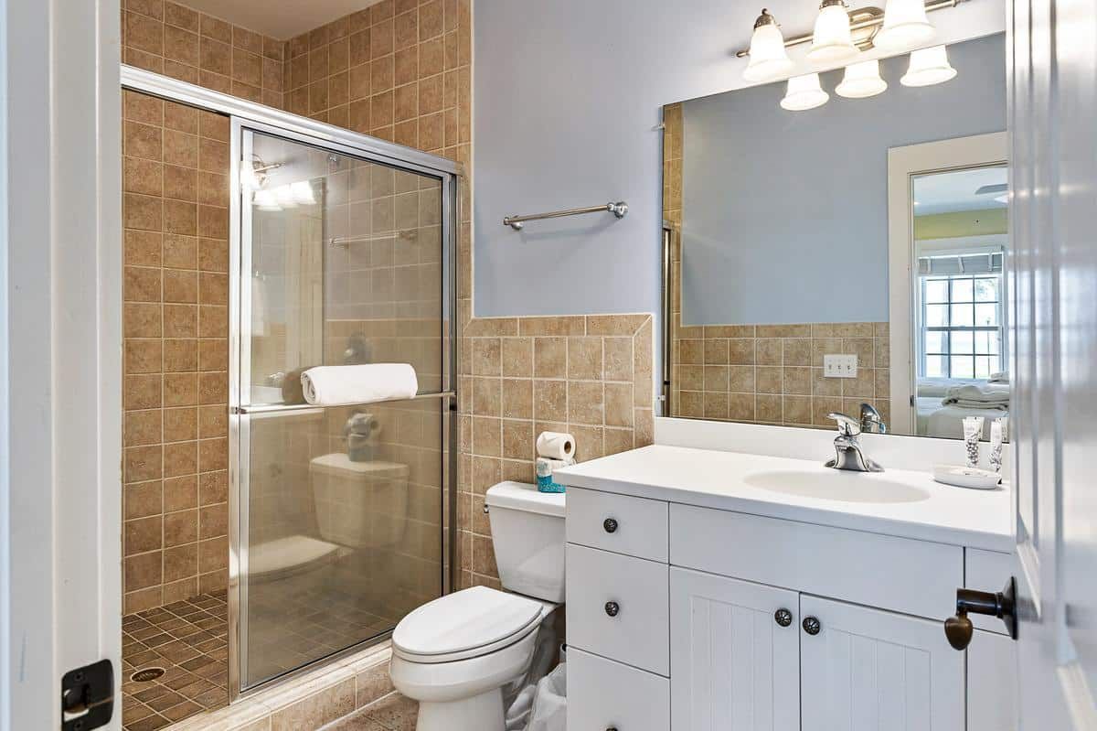 A bathroom with a toilet , sink , mirror and shower.