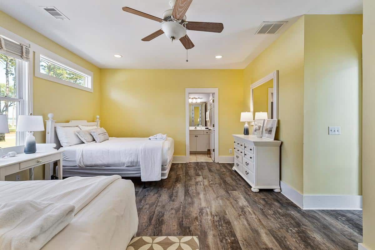 A bedroom with two beds , a dresser , a mirror and a ceiling fan.