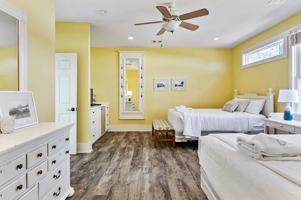 A bedroom with two beds , a dresser , a mirror and a ceiling fan.