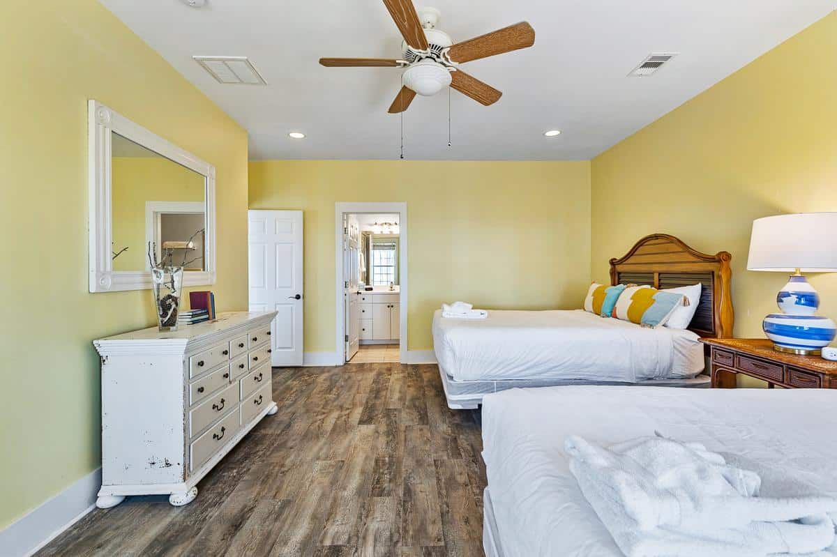 A bedroom with two beds , a dresser , a mirror and a ceiling fan.
