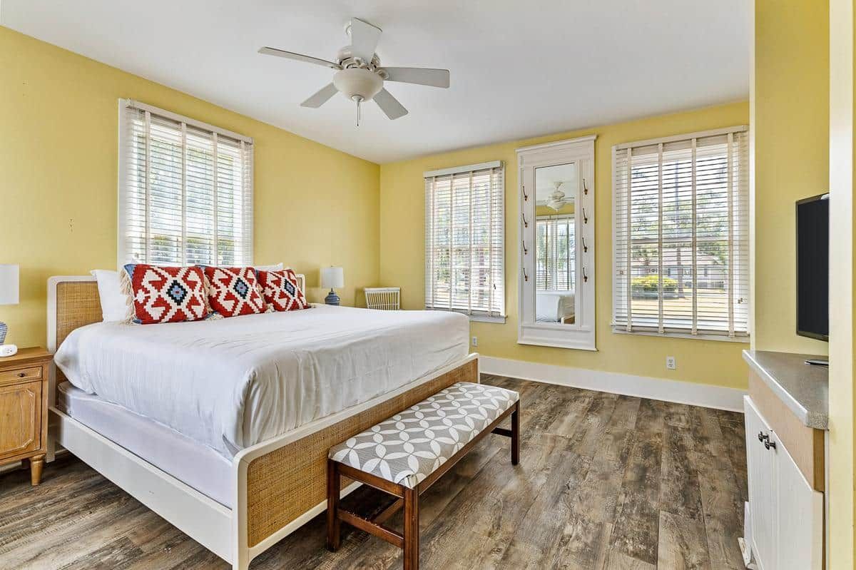 A bedroom with a king size bed , a bench , a television and a ceiling fan.