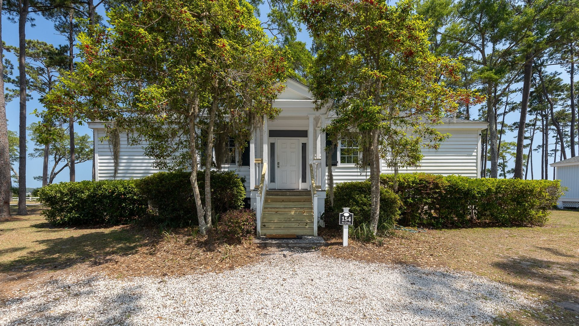 A white house is surrounded by trees and a gravel driveway.
