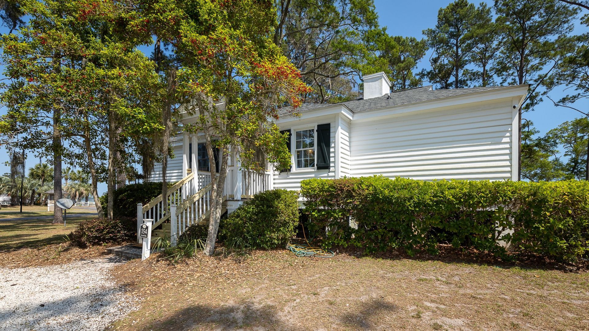 A white house is surrounded by trees and bushes on a sunny day.