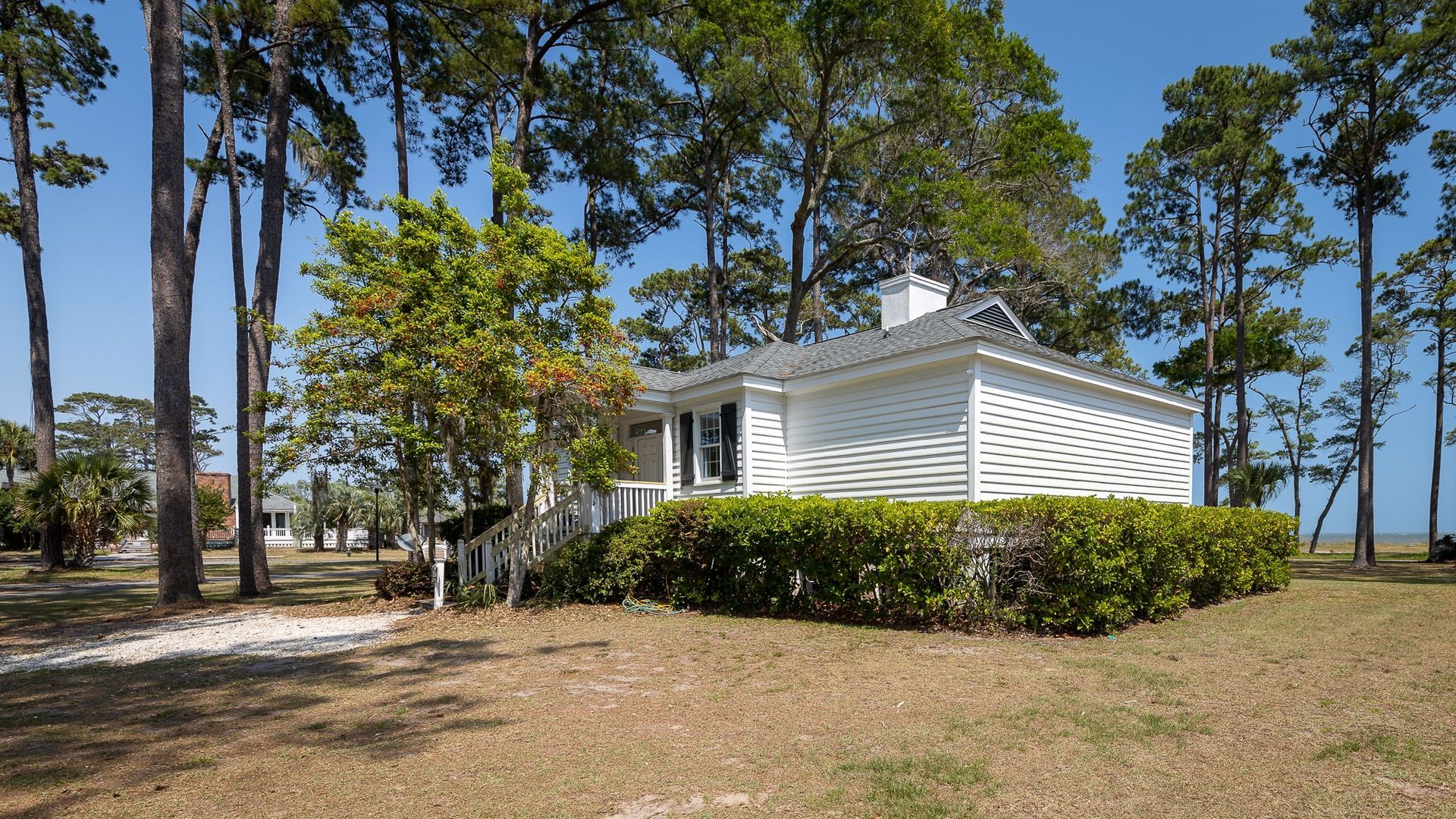 A small white house is surrounded by trees on a sunny day