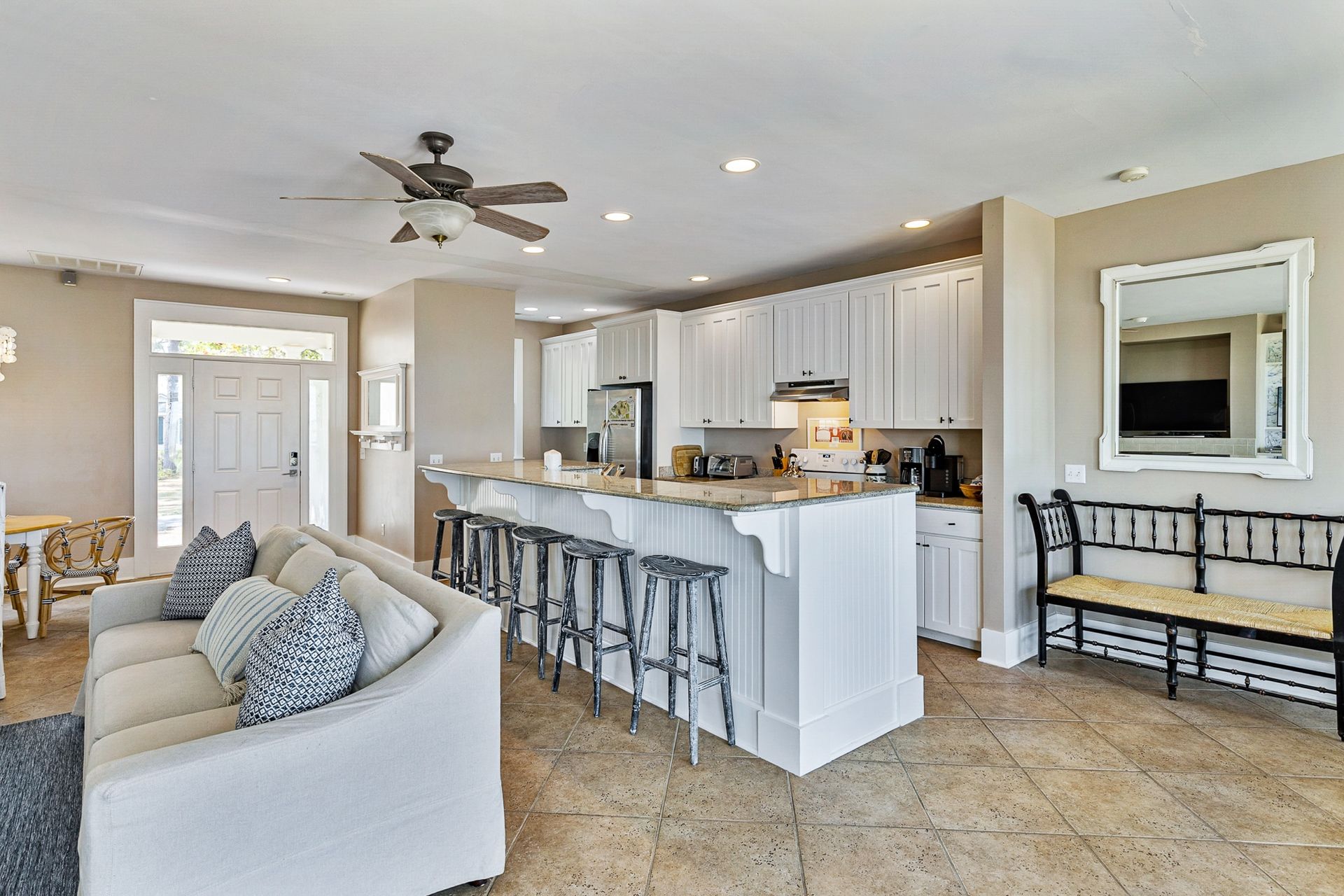 A living room with a couch , chairs , and a kitchen with a ceiling fan.