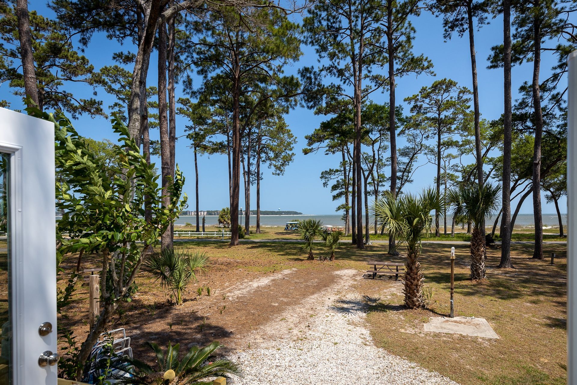 A white door is open to a dirt path leading to the ocean.