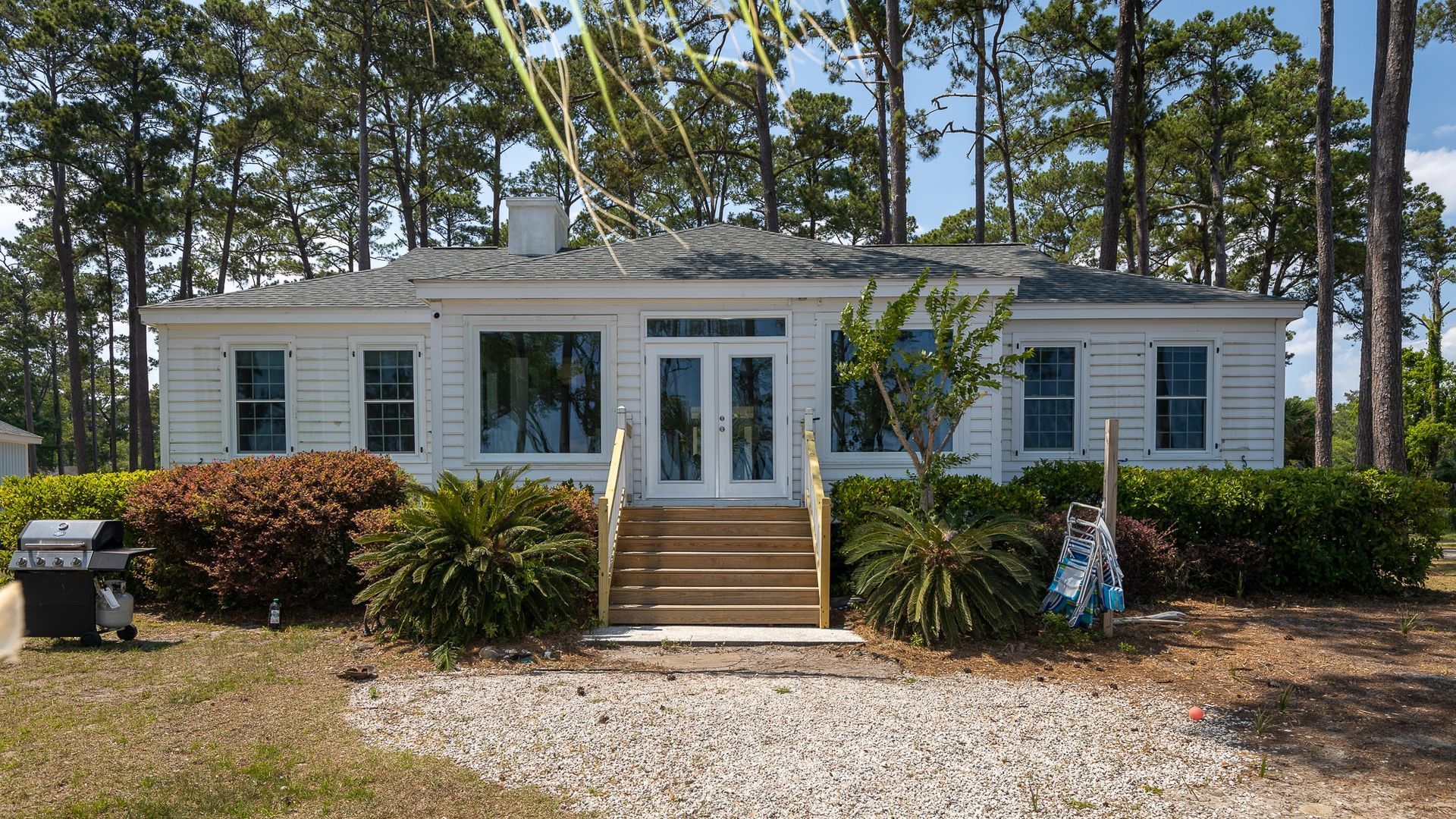 A white house with a grill in front of it is surrounded by trees.