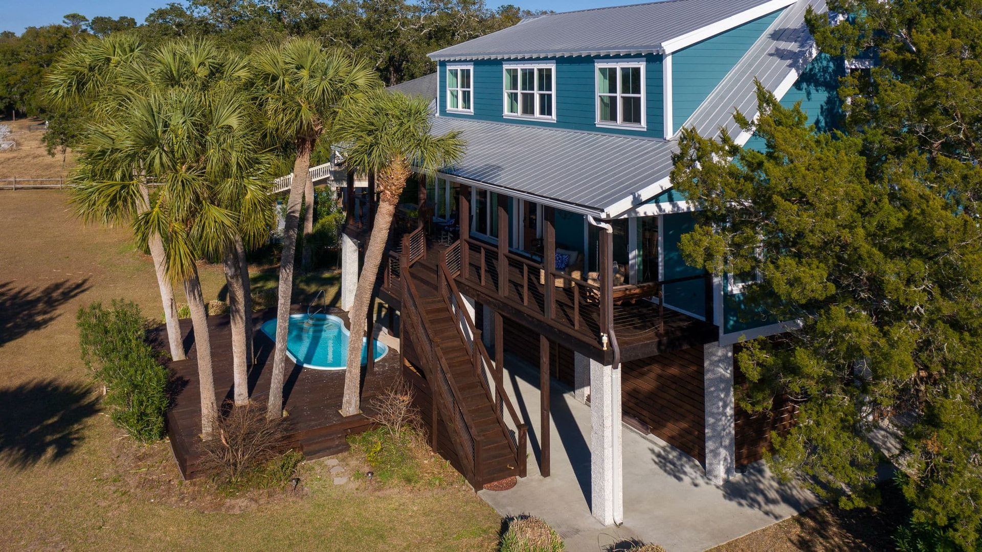 An aerial view of a blue house with a pool in the backyard surrounded by trees.