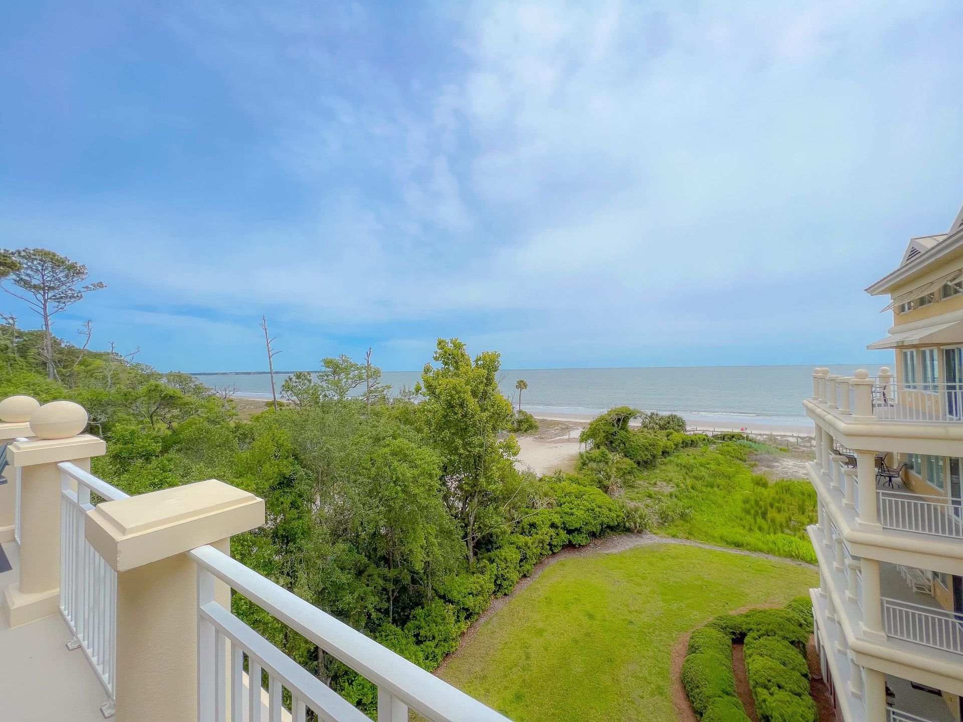A balcony with a view of the ocean and a lush green field.