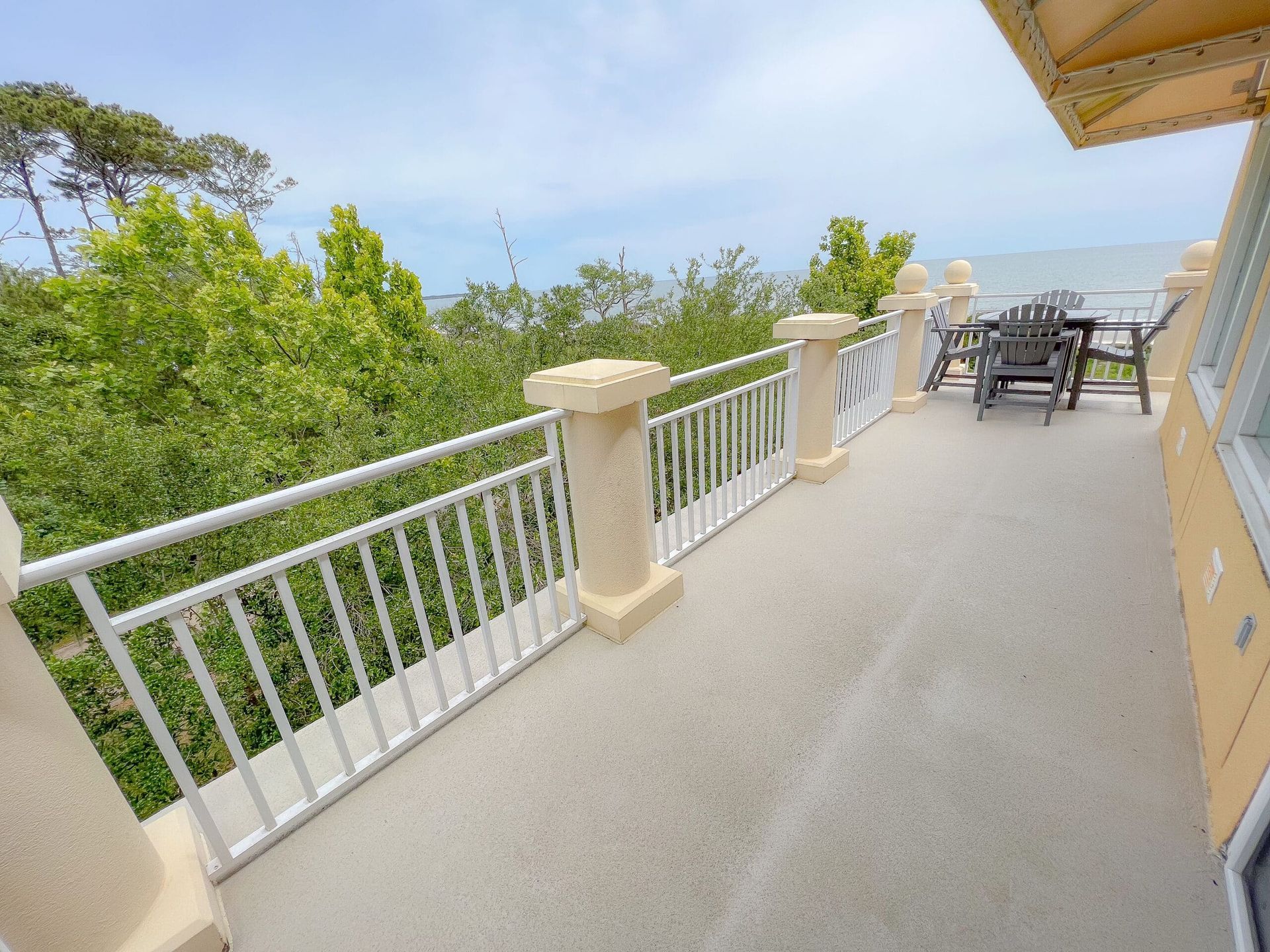 There is a balcony with a view of the ocean and trees.