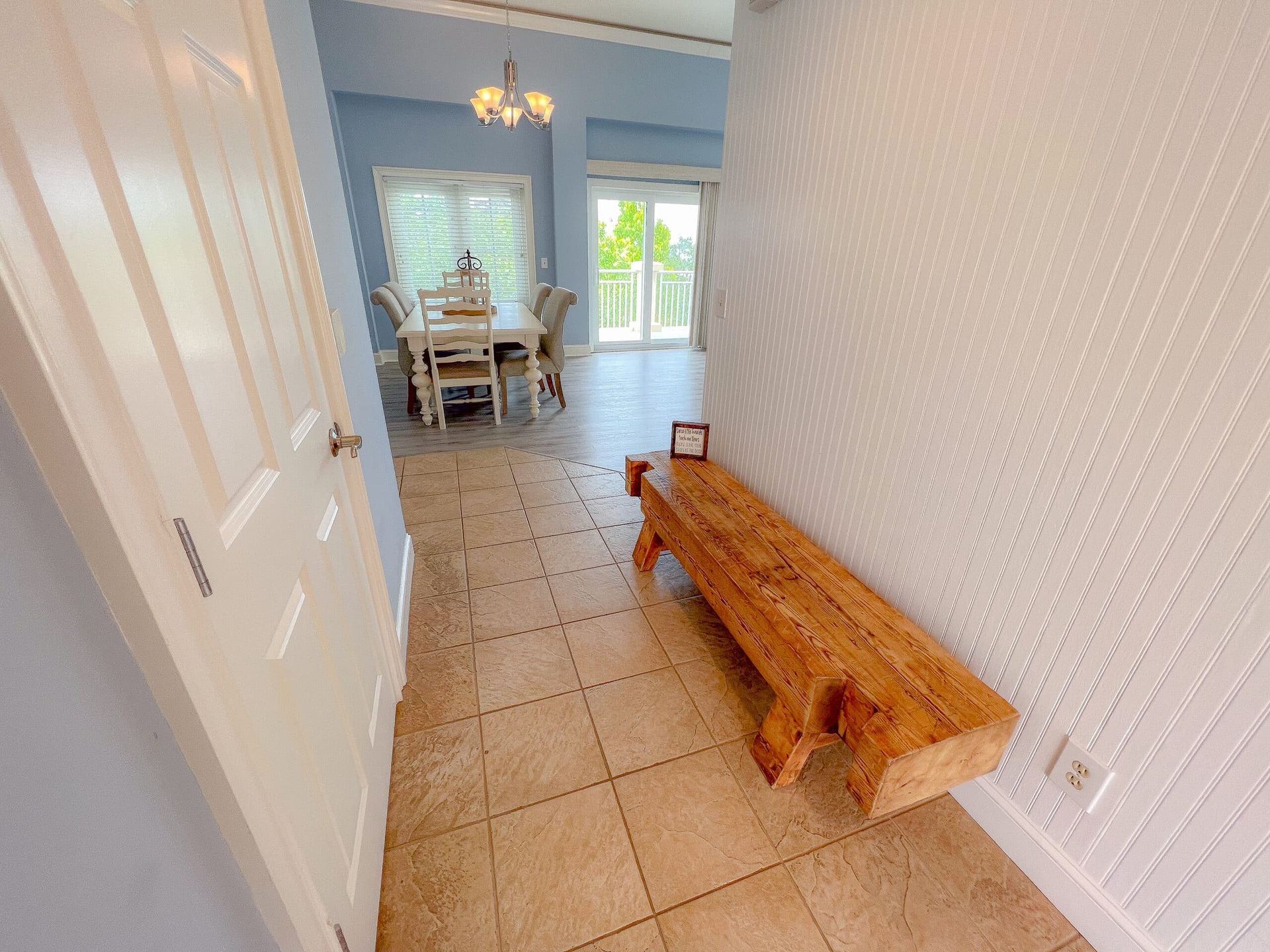 A hallway with a wooden bench in the middle of it leading to a dining room.
