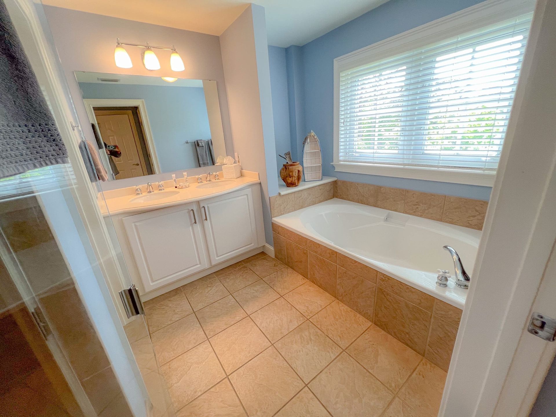 A bathroom with a tub , sink , mirror and window.