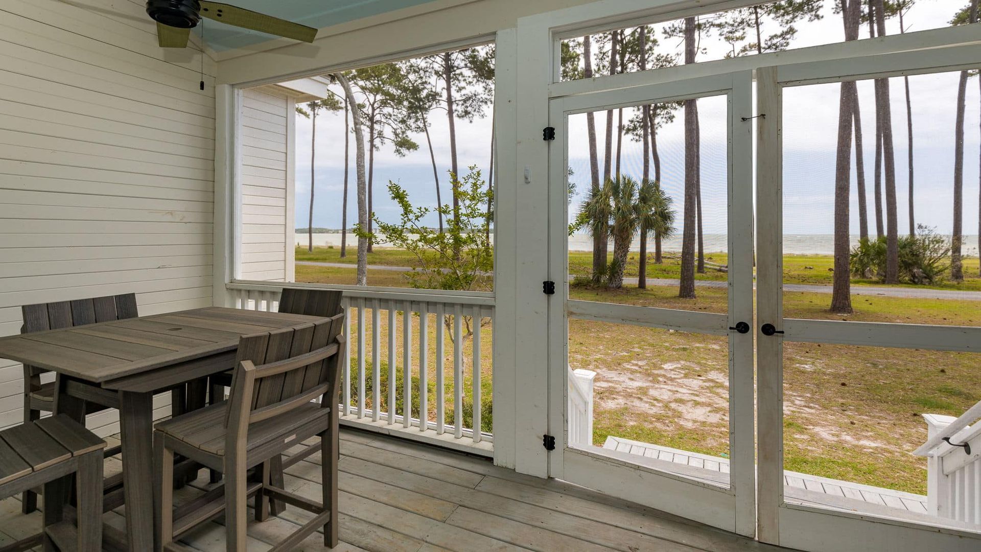 A screened in porch with a table and chairs and a view of the ocean.