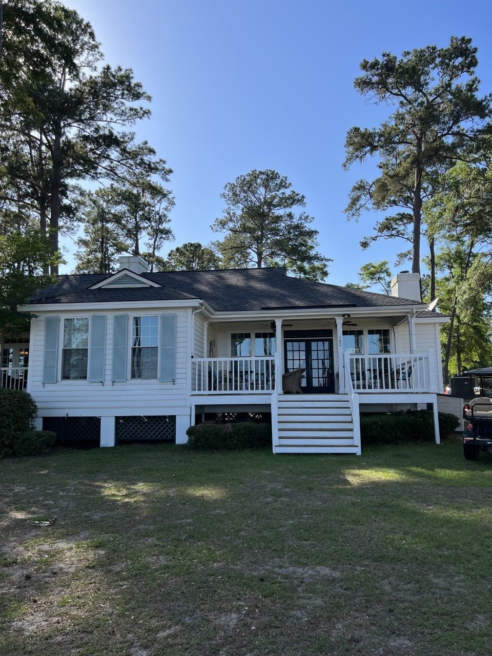 A white house with a black roof is surrounded by trees