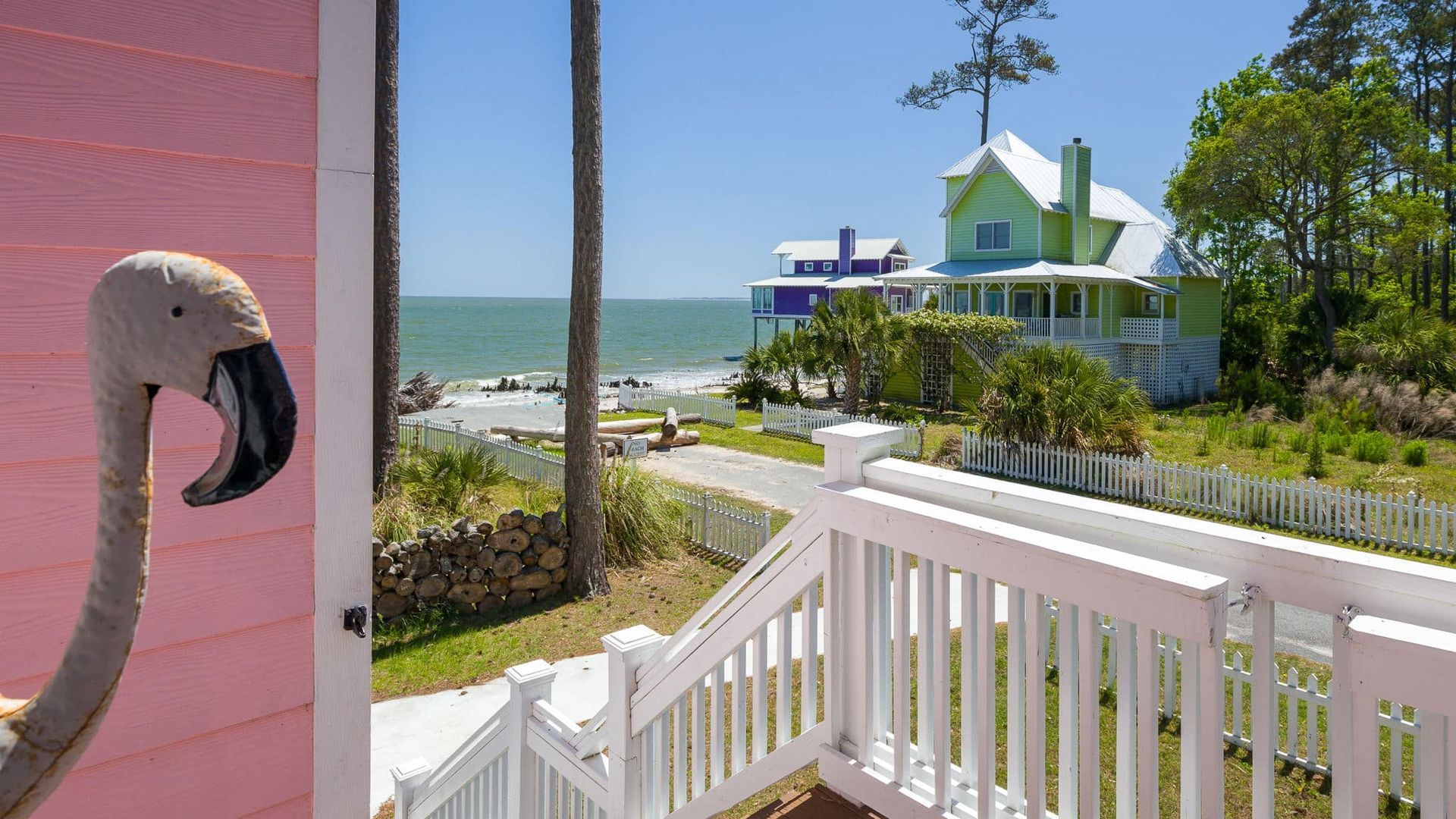 A stuffed flamingo is sitting on a door next to a balcony overlooking the ocean.