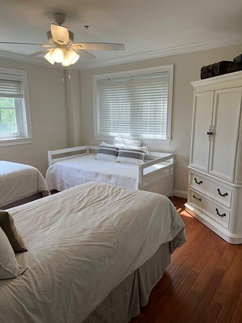 A bedroom with two beds , a dresser , and a ceiling fan.