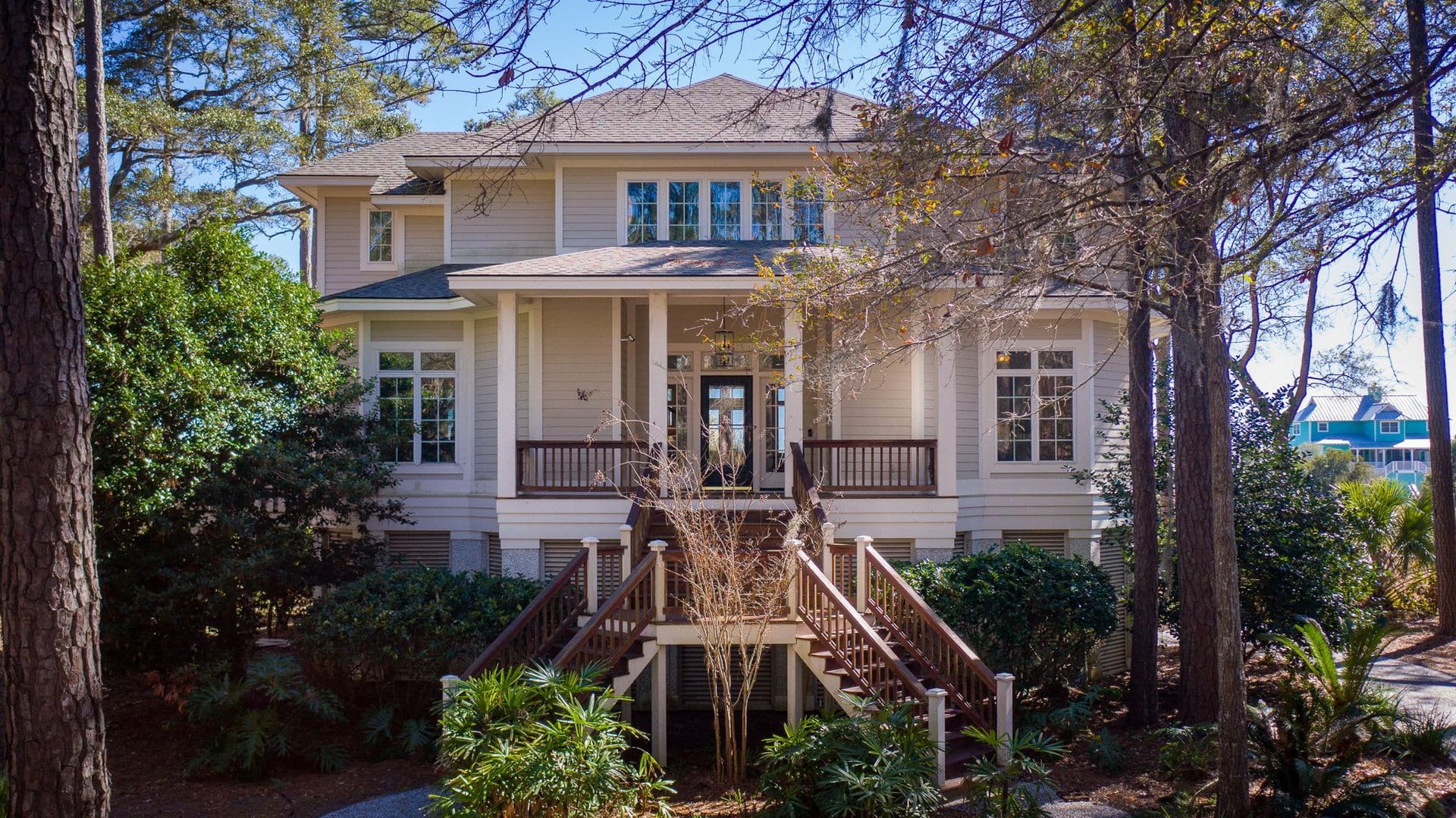 A large white house with stairs leading up to it is surrounded by trees.