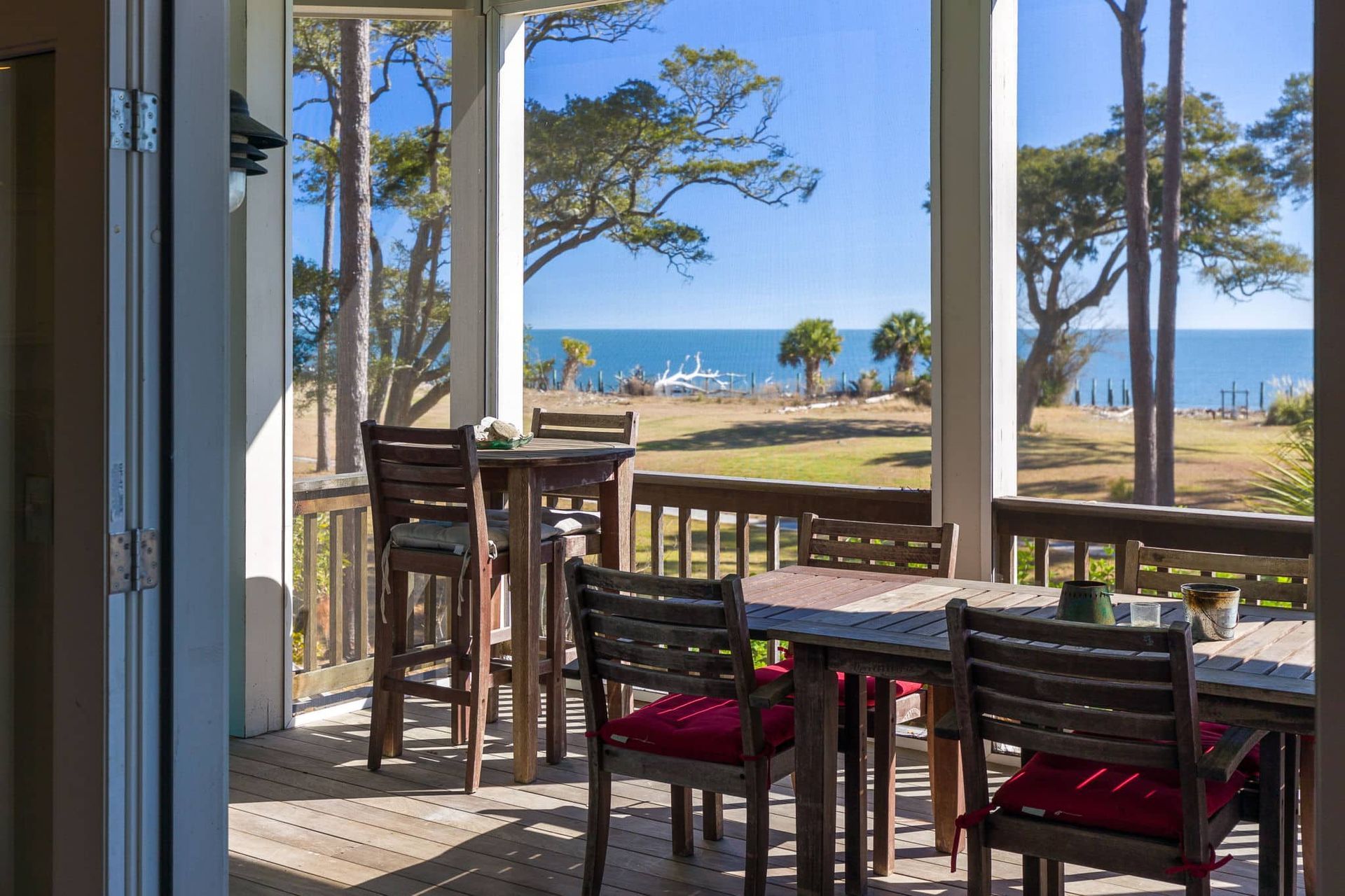 A screened in porch with a table and chairs overlooking the ocean.
