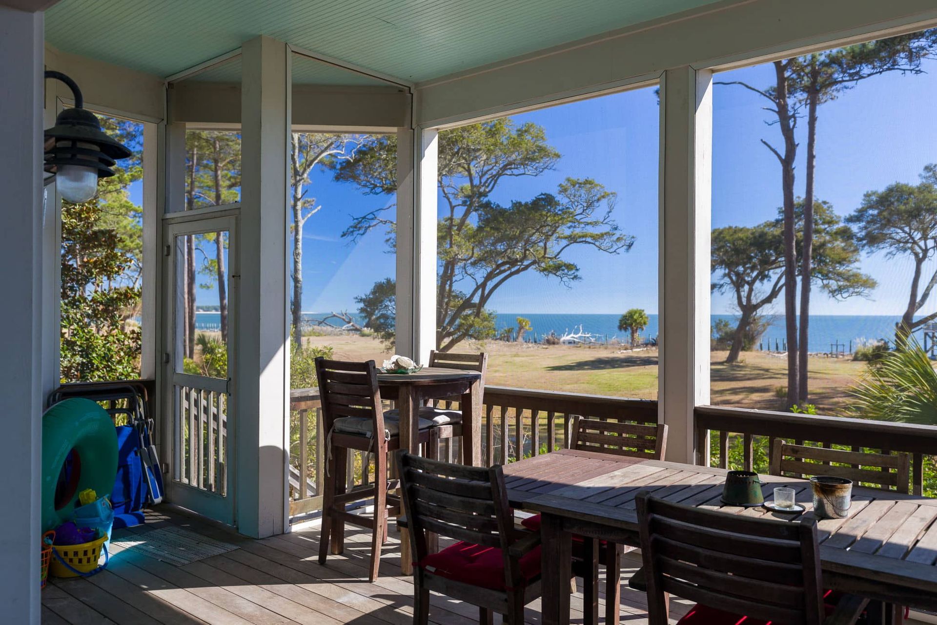 A screened in porch with a table and chairs overlooking the ocean.