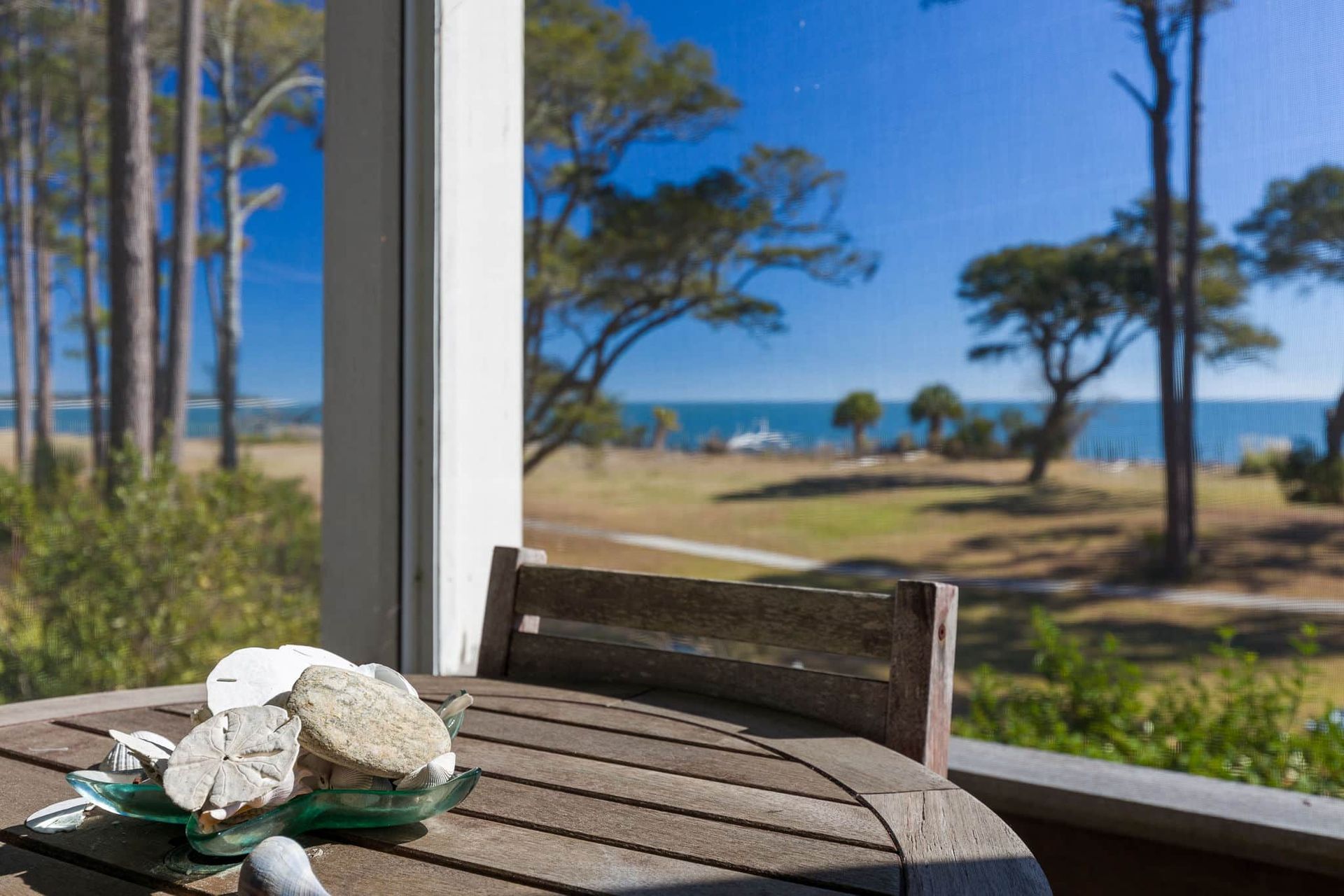 A wooden table with seashells on it and a view of the ocean.