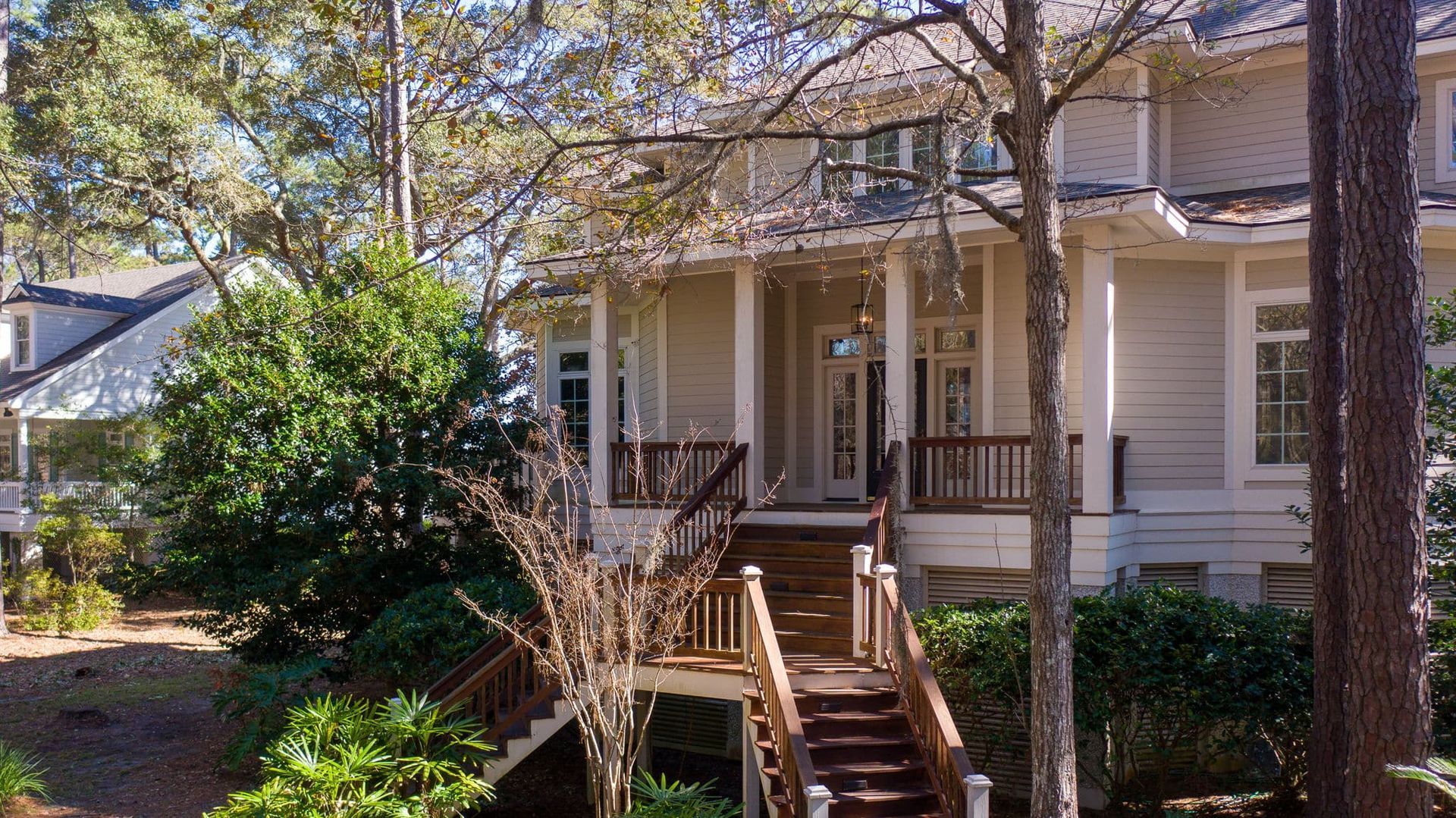 A large white house with a wooden deck and stairs surrounded by trees.