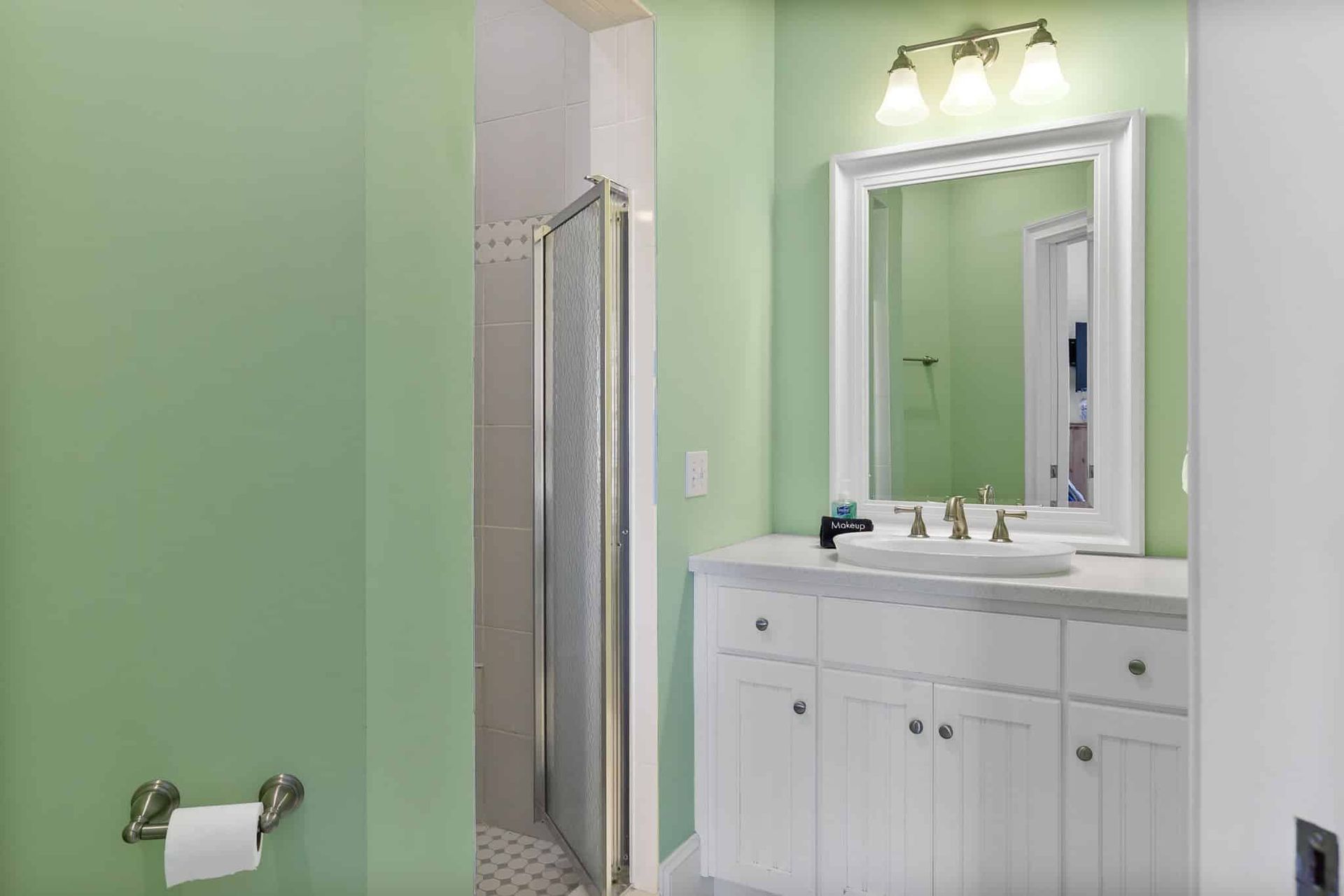 A bathroom with green walls , white cabinets , a sink and a mirror.