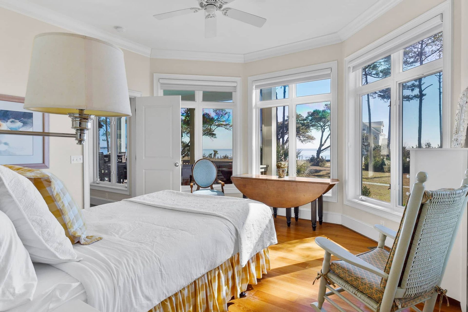A bedroom with a large bed , rocking chair , lamp and lots of windows.