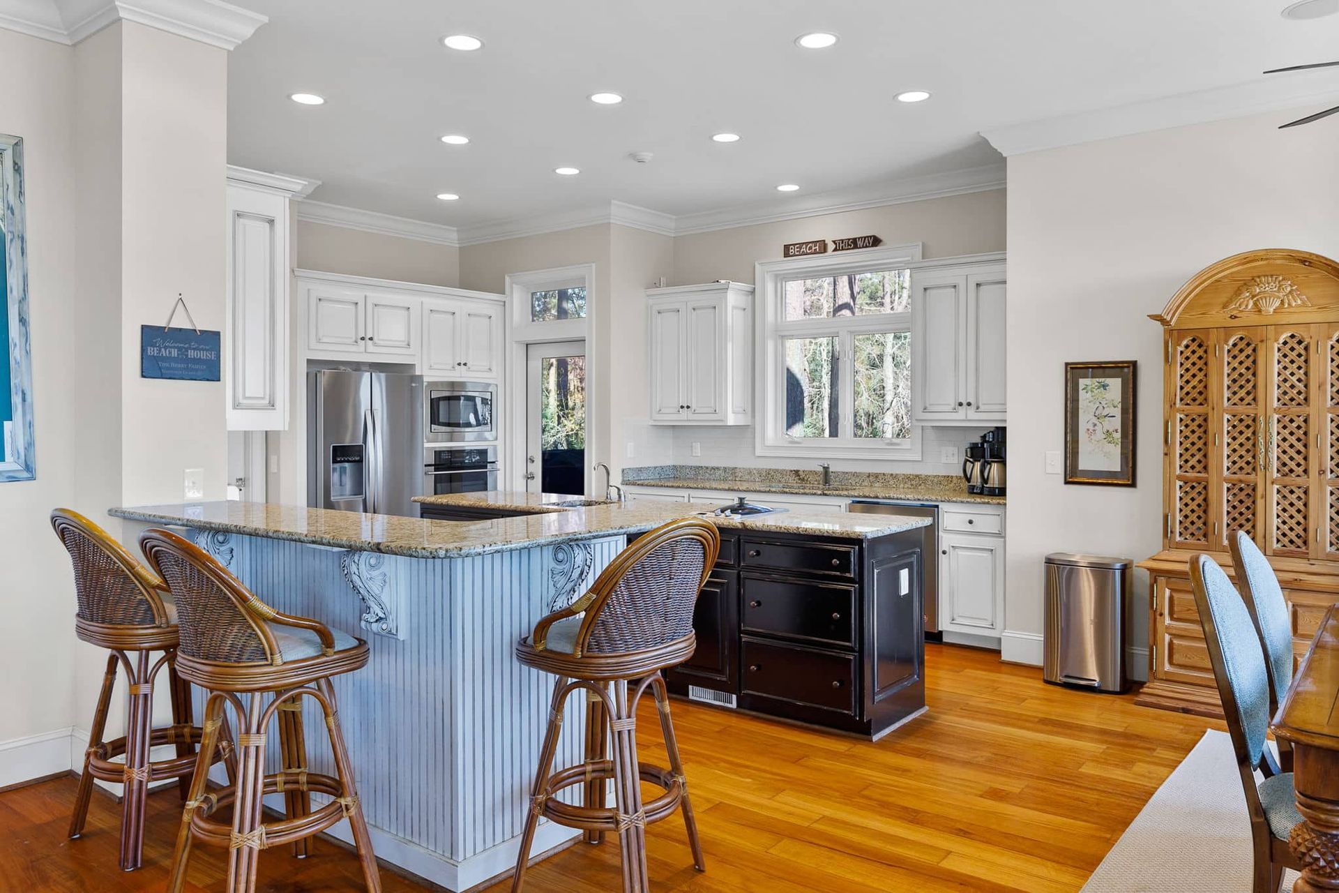A kitchen with a large island , stools , a refrigerator and a dishwasher.