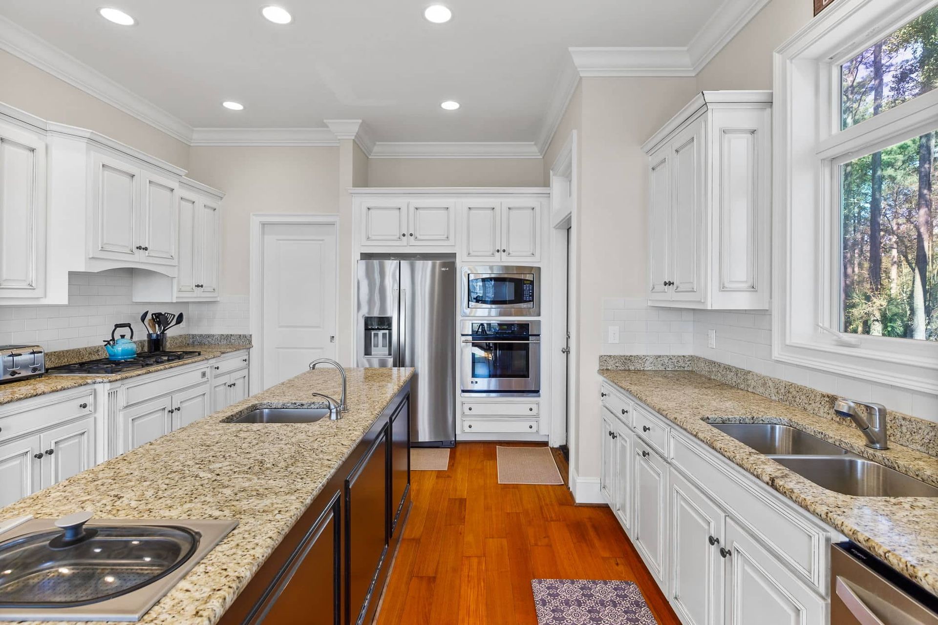 A kitchen with granite counter tops , stainless steel appliances , white cabinets and hardwood floors.