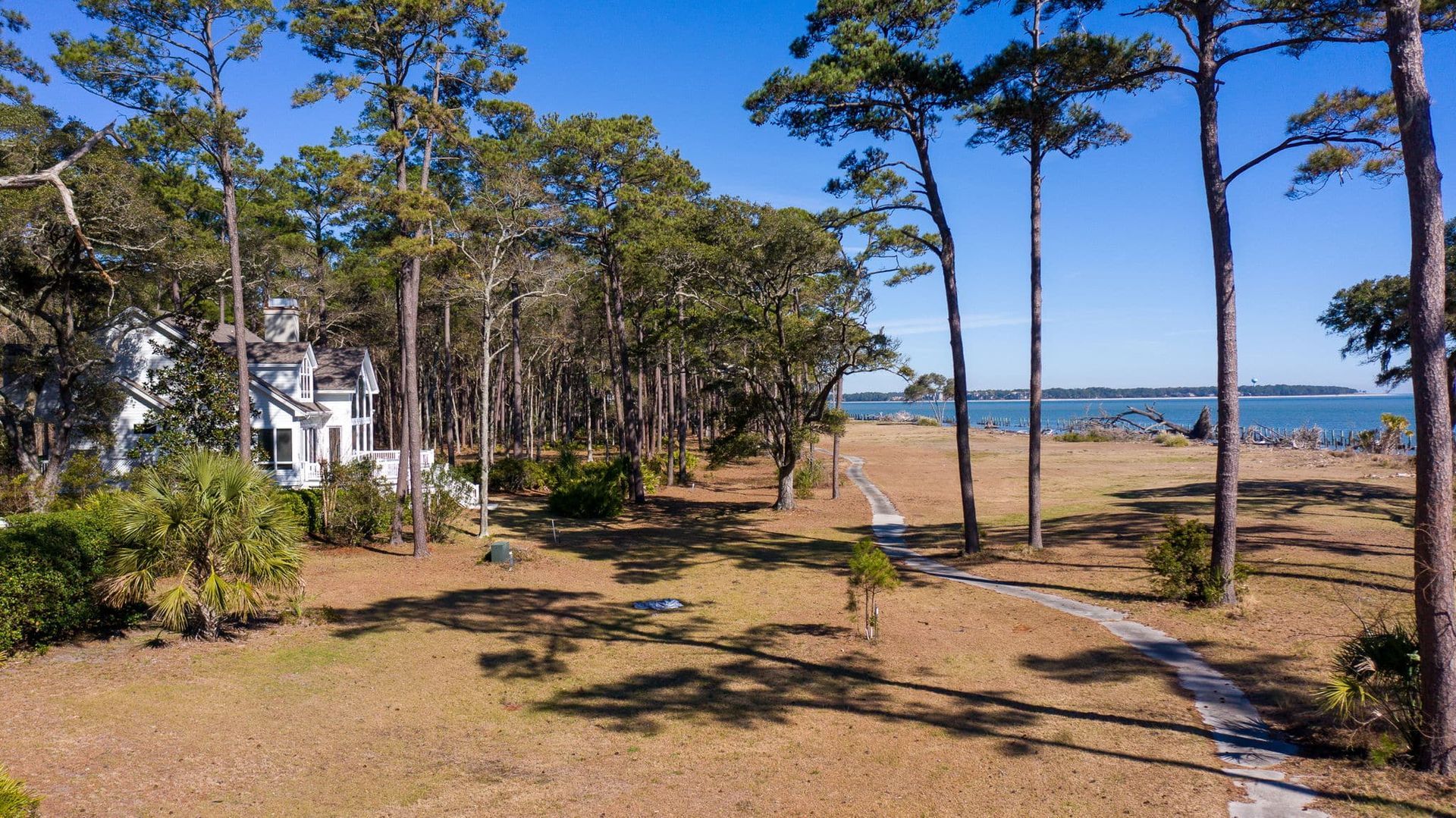 An aerial view of a house surrounded by trees and a path leading to the ocean.