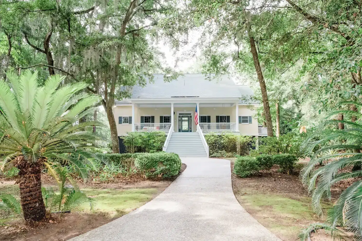 A white house with a walkway leading to it is surrounded by trees.