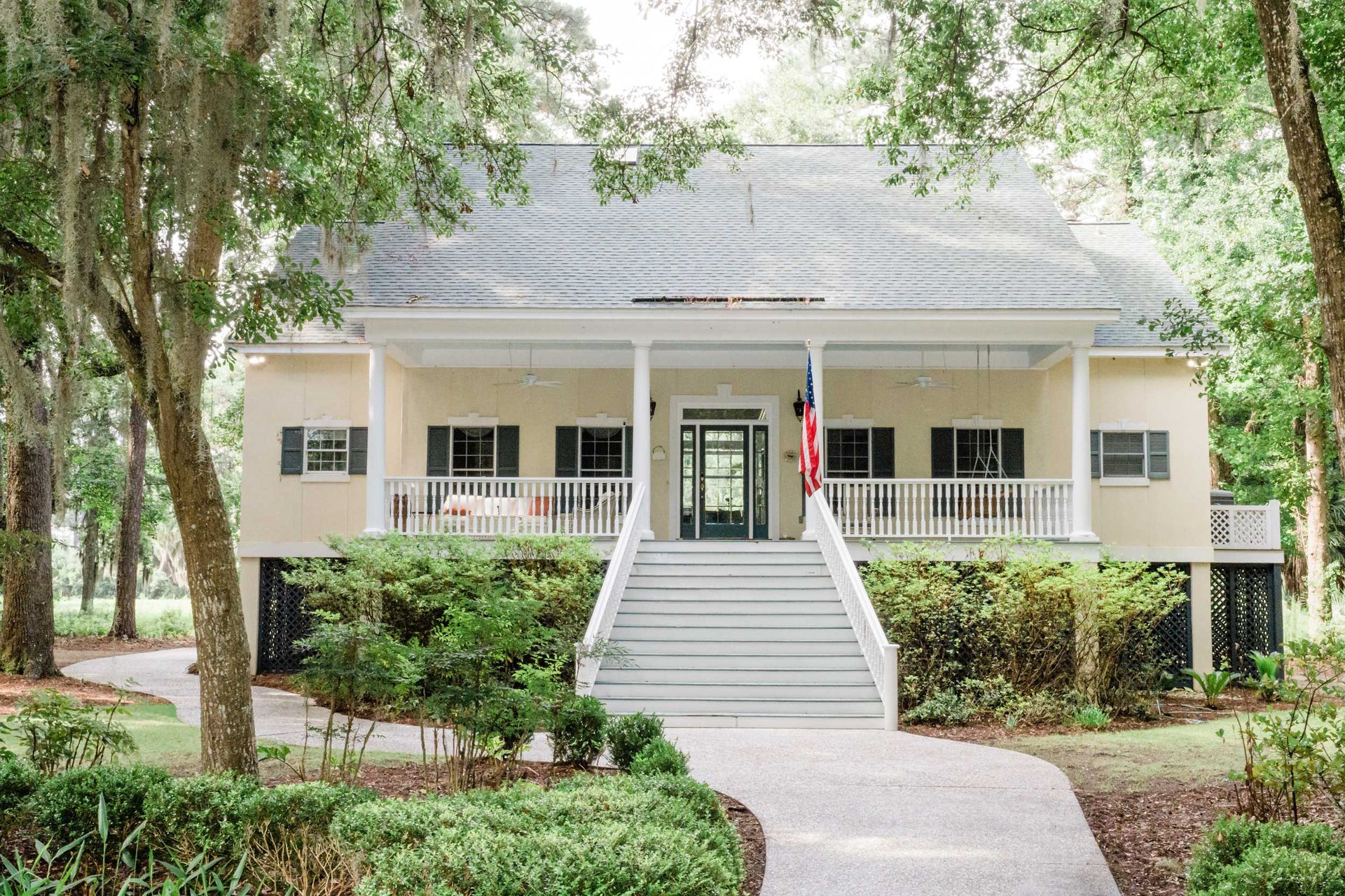 A large house with a large porch and stairs is surrounded by trees.
