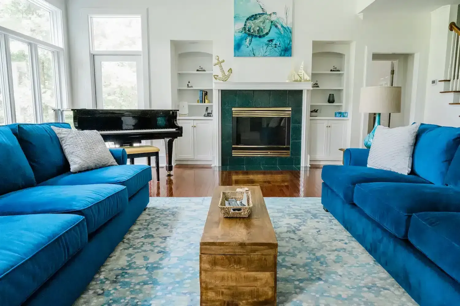 A living room with two blue couches , a piano , and a fireplace.