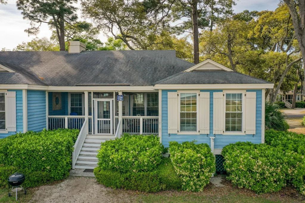 A blue house with white shutters and a grill in front of it