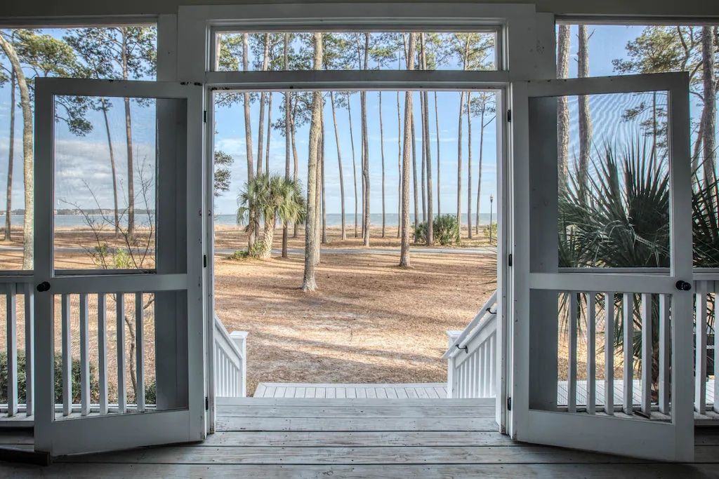 A screened in porch with a view of a forest and the ocean.