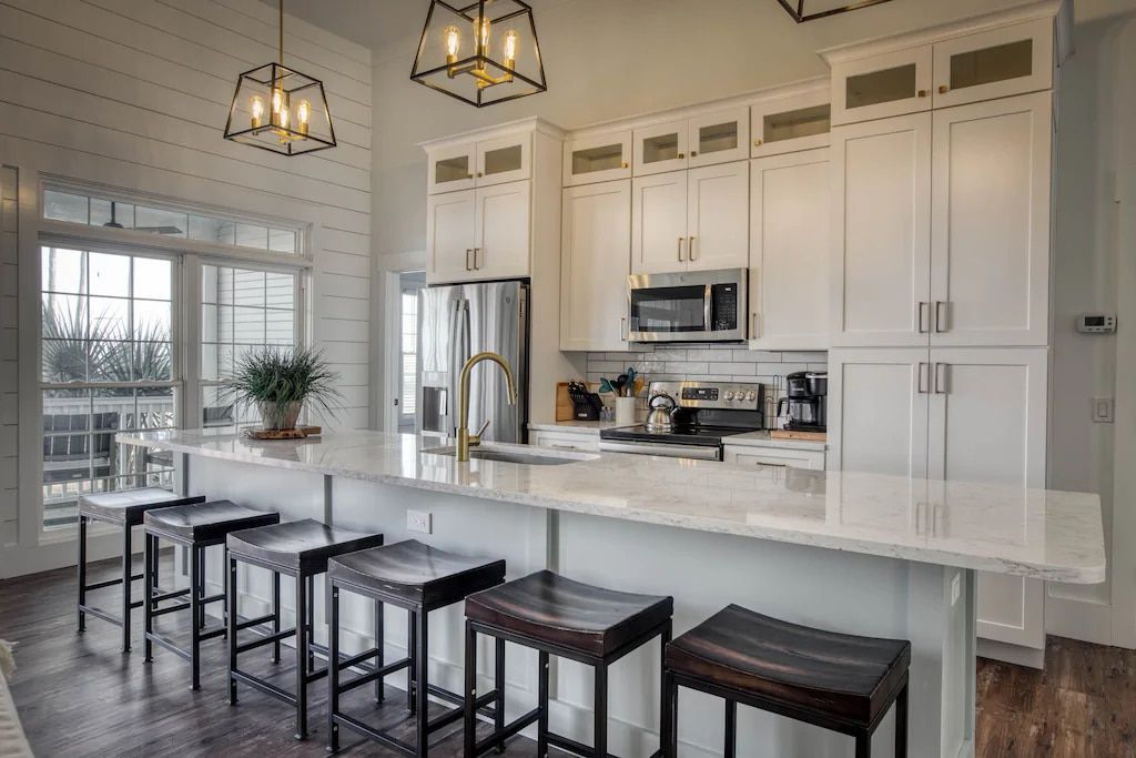A kitchen with white cabinets , stools and a large island.