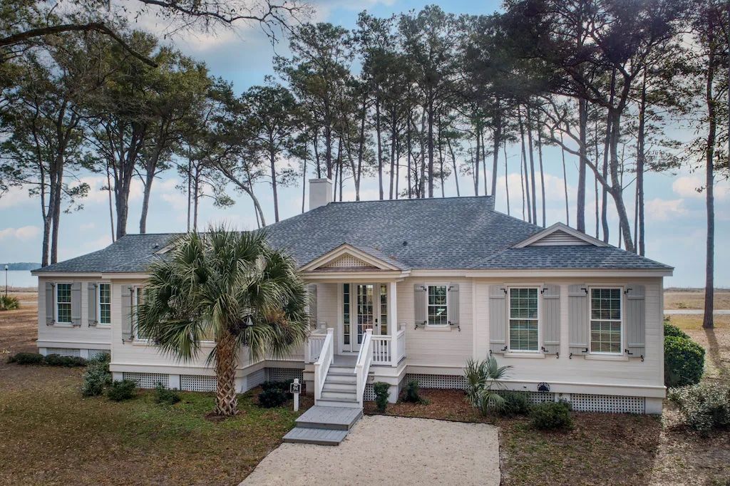 A white house with a blue roof is surrounded by trees