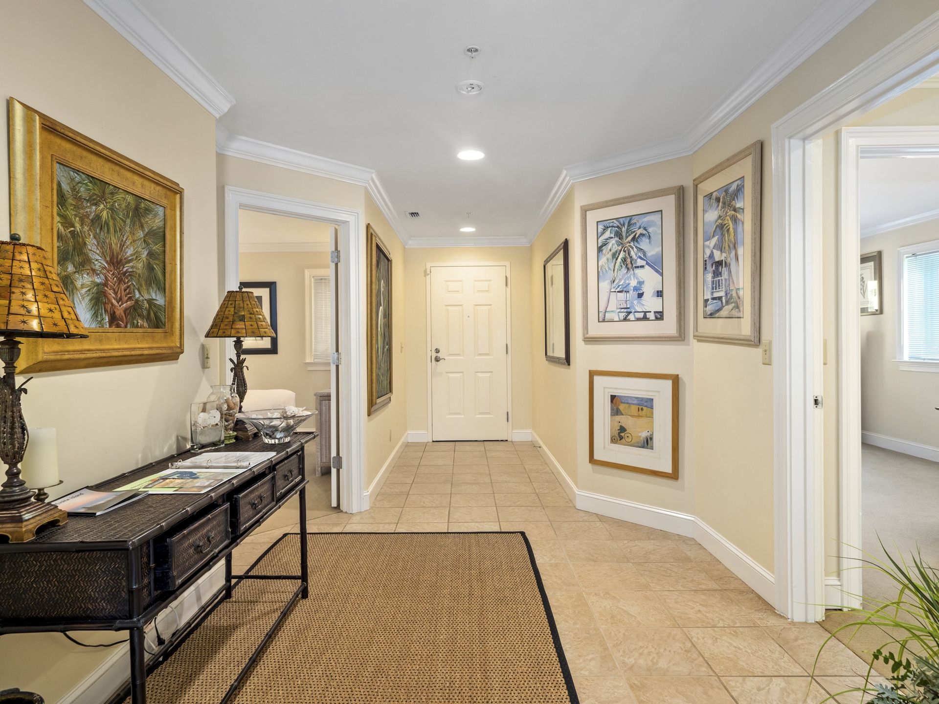 A hallway with a table , lamps , and paintings on the wall.