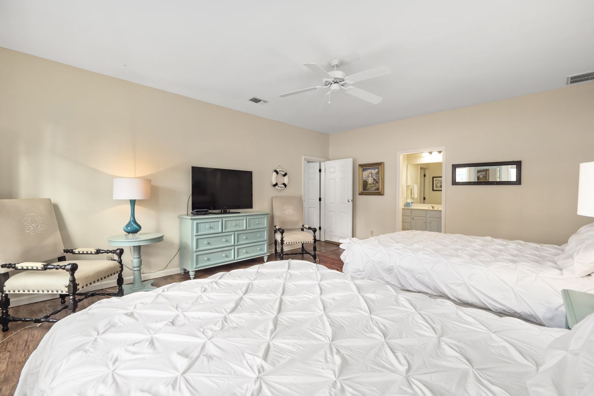 A bedroom with two beds , a dresser , chairs , a television and a ceiling fan.