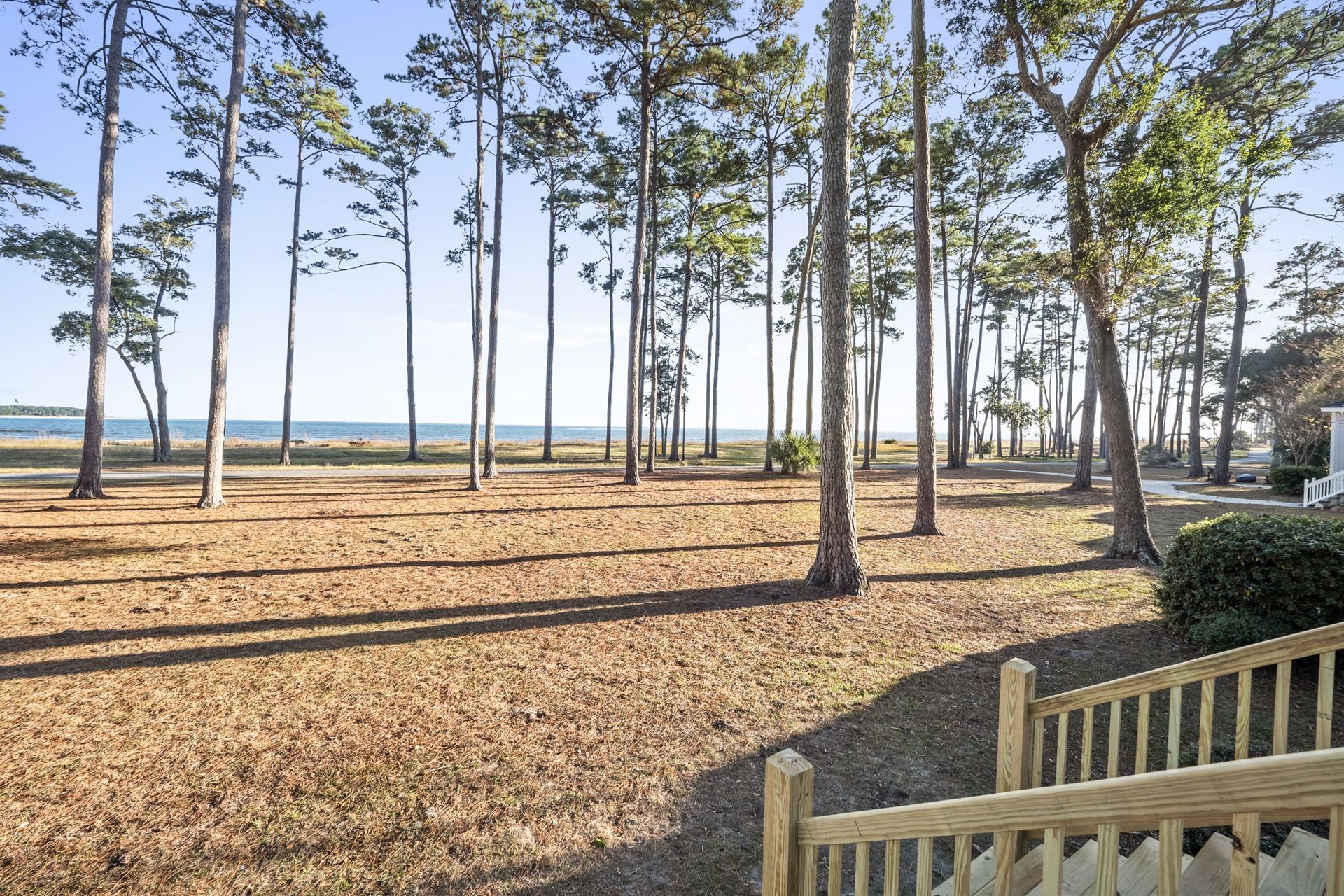 A wooden fence surrounds a field with trees and a view of the ocean.