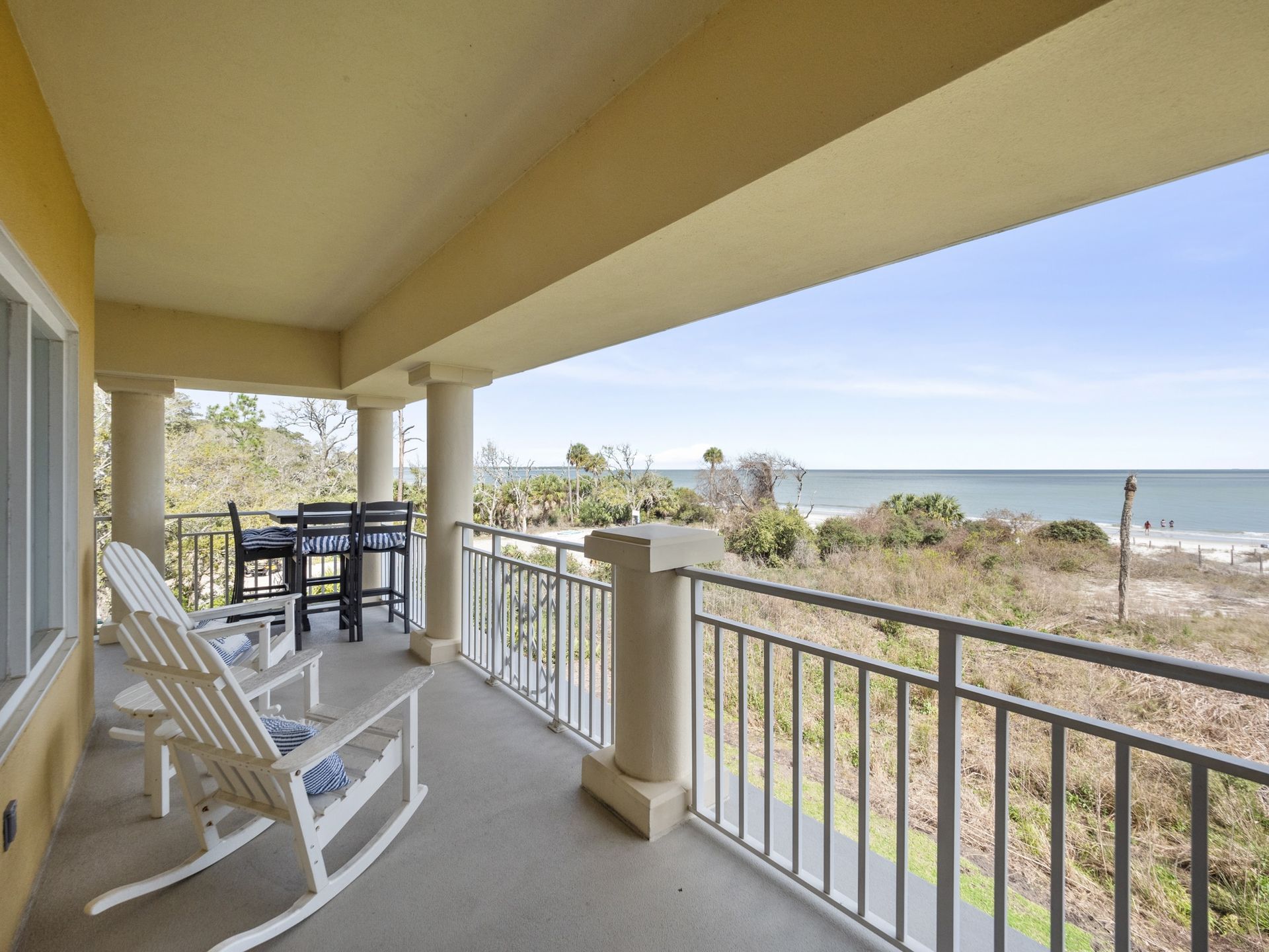 A balcony with rocking chairs and a table overlooking the ocean