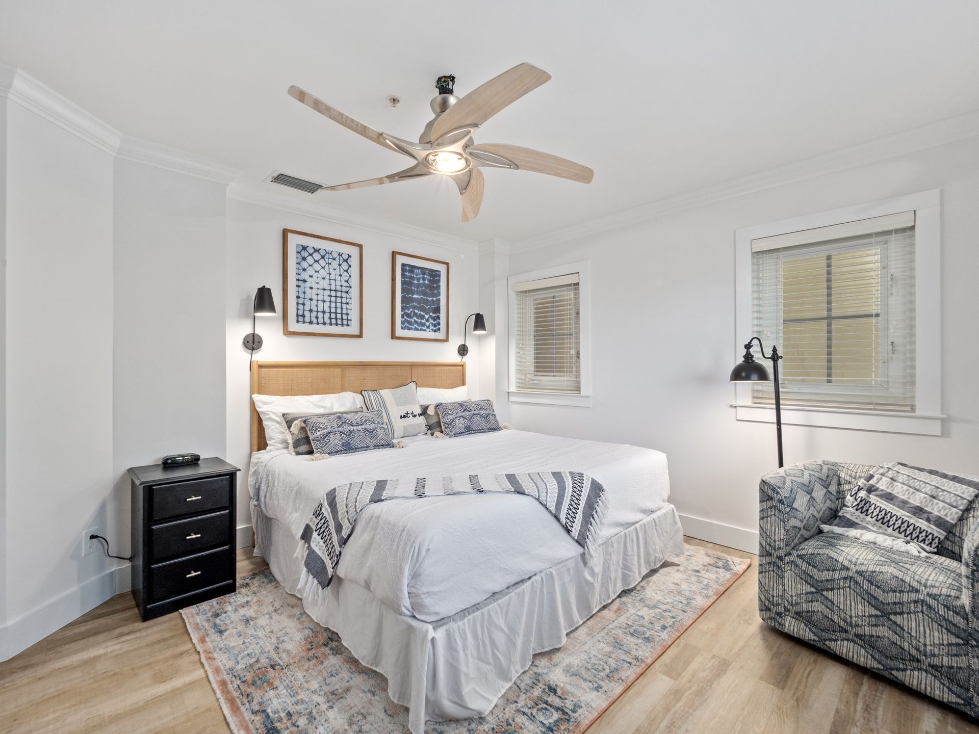 A bedroom with a bed , chair , nightstand and ceiling fan.