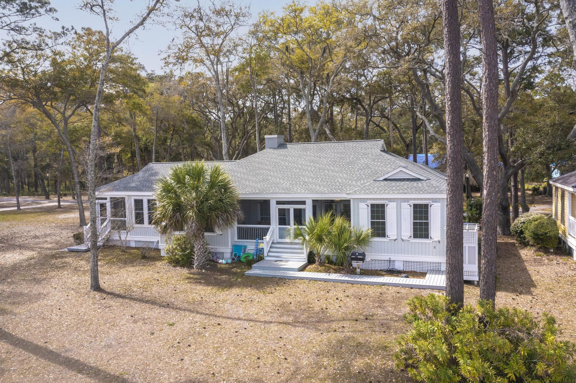 A white house with a screened in porch is surrounded by trees.