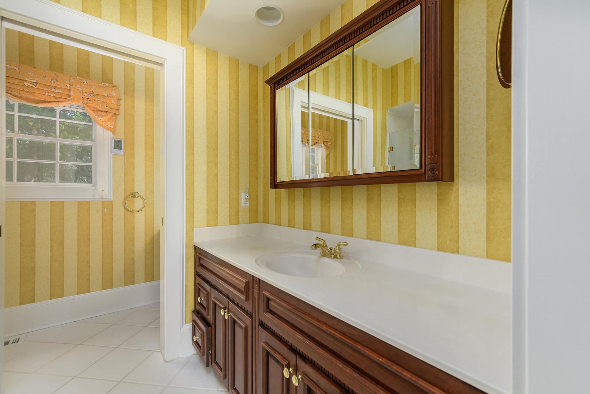A bathroom with a sink , mirror and striped wallpaper.